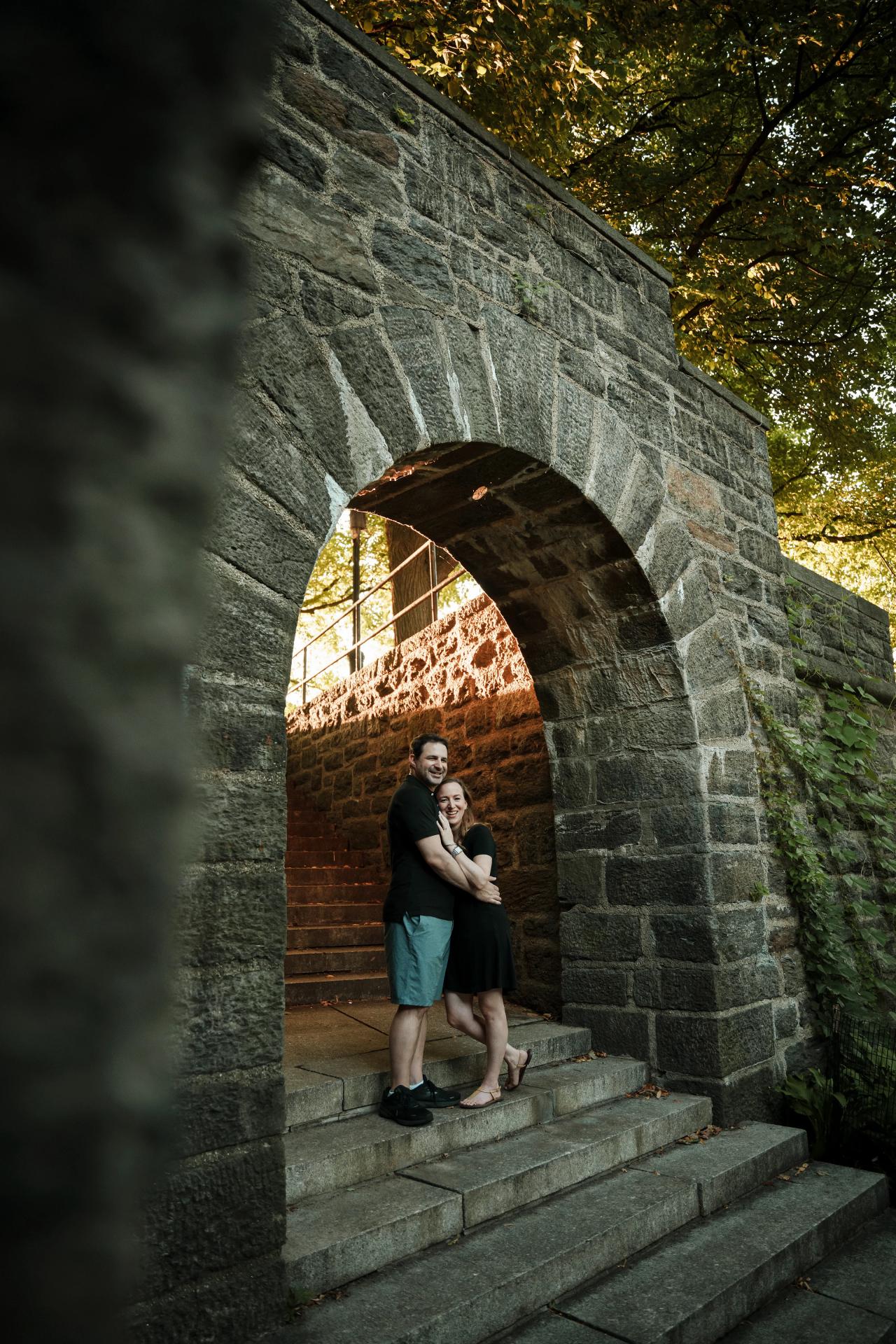 Engagement portrait seen through a stone arch and foreground wall