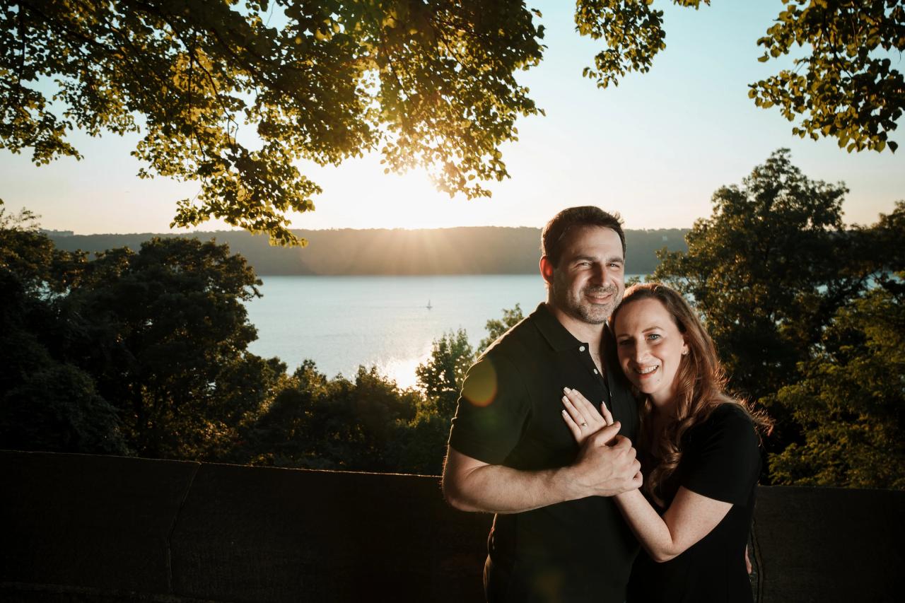 Wide portrait of an engaged couple with sunlit water behind them