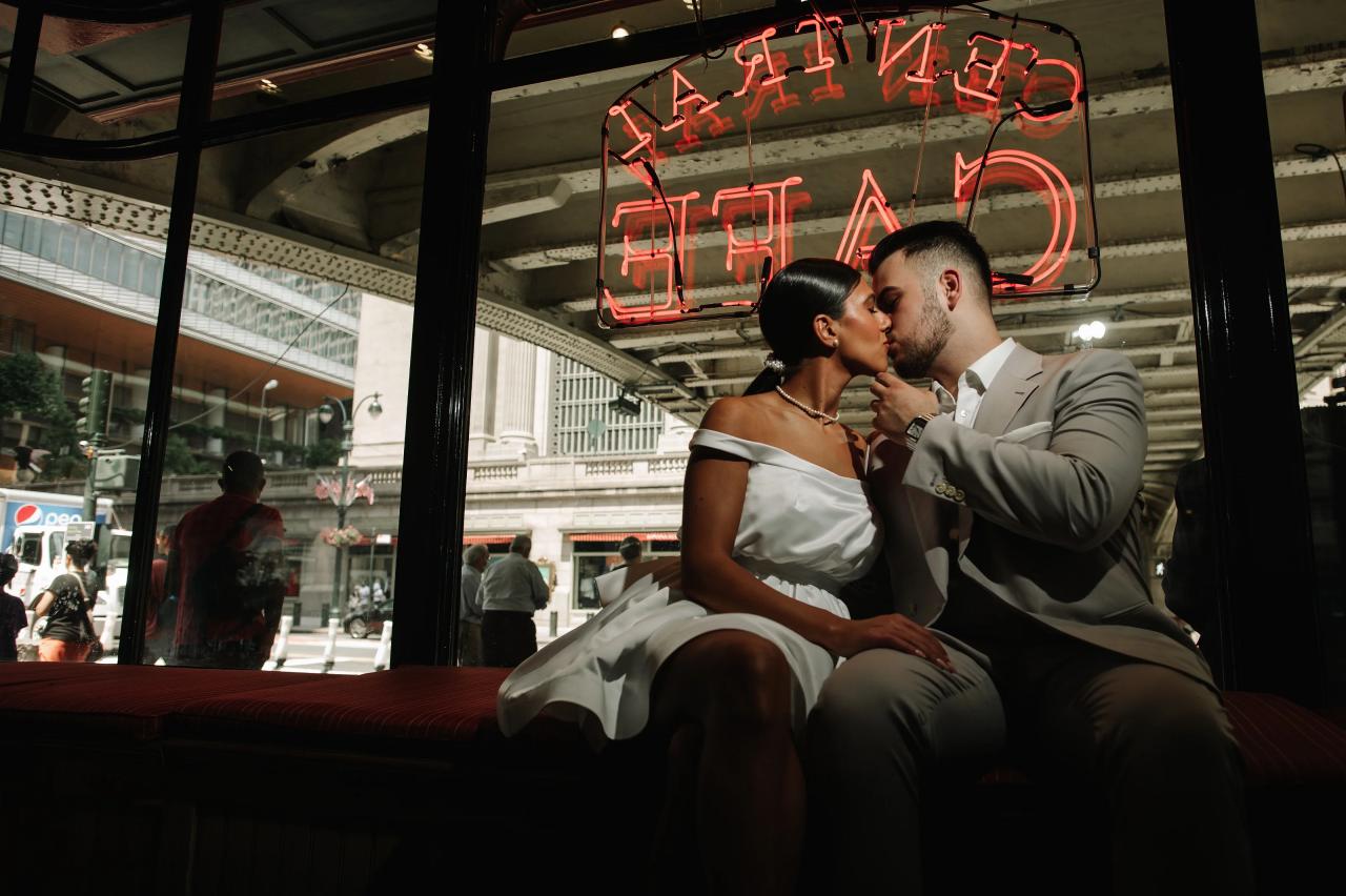 Couple kissing beneath a red cafe sign beside a city window