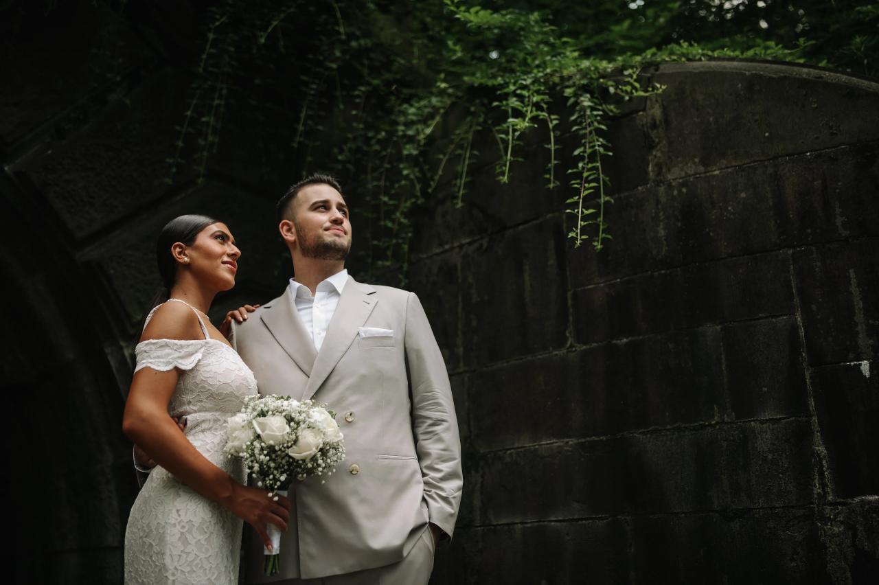 Engaged couple standing beside an ivy-covered stone wall in Central Park