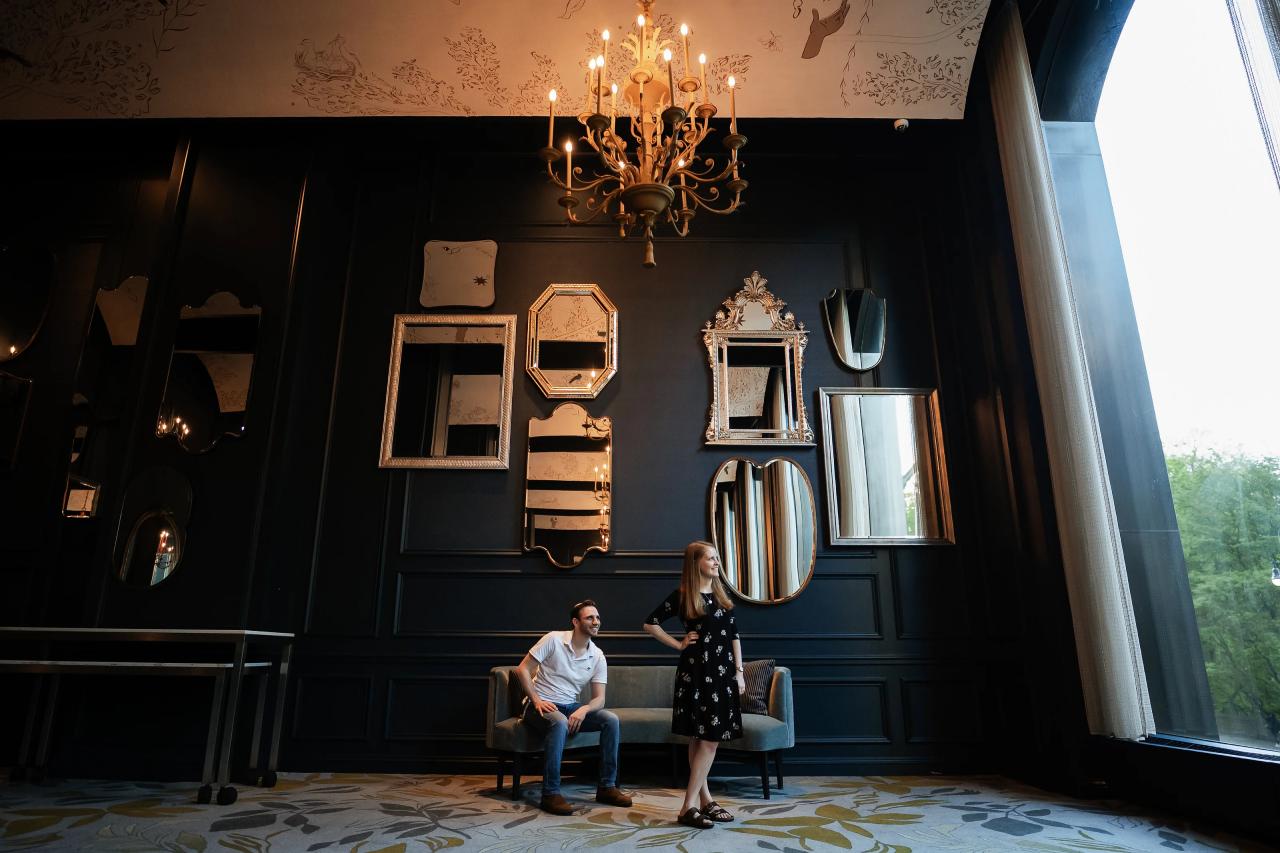 Wide engagement portrait in a dark blue room with mirrors and a chandelier
