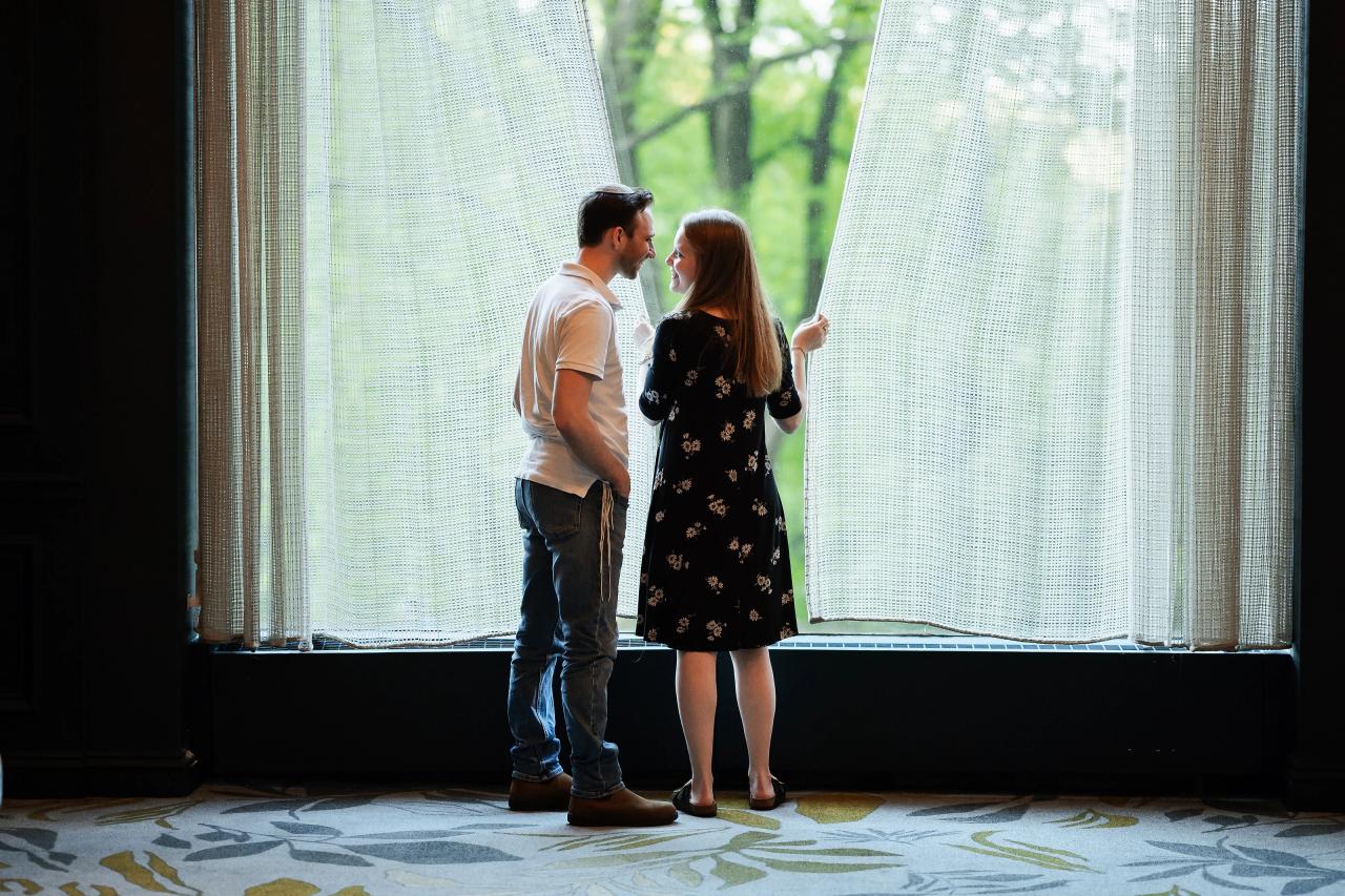Couple facing each other beside a tall window