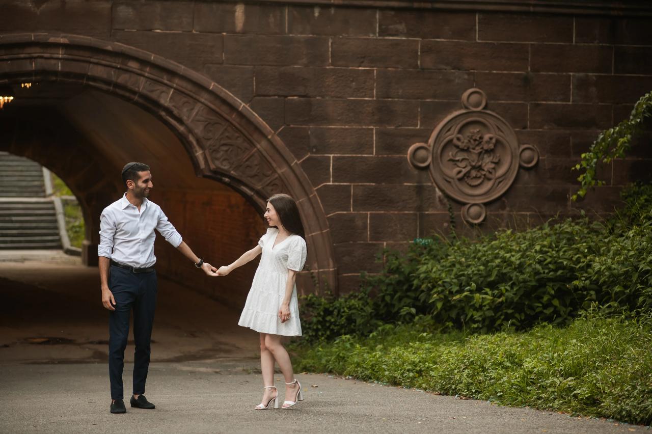 Couple holding hands beside a park archway