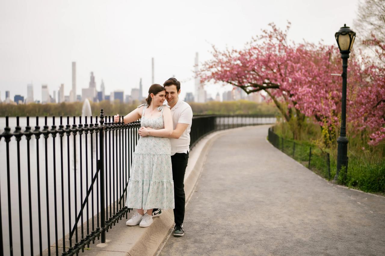 Couple embracing beside the lake with pink spring blossoms behind them