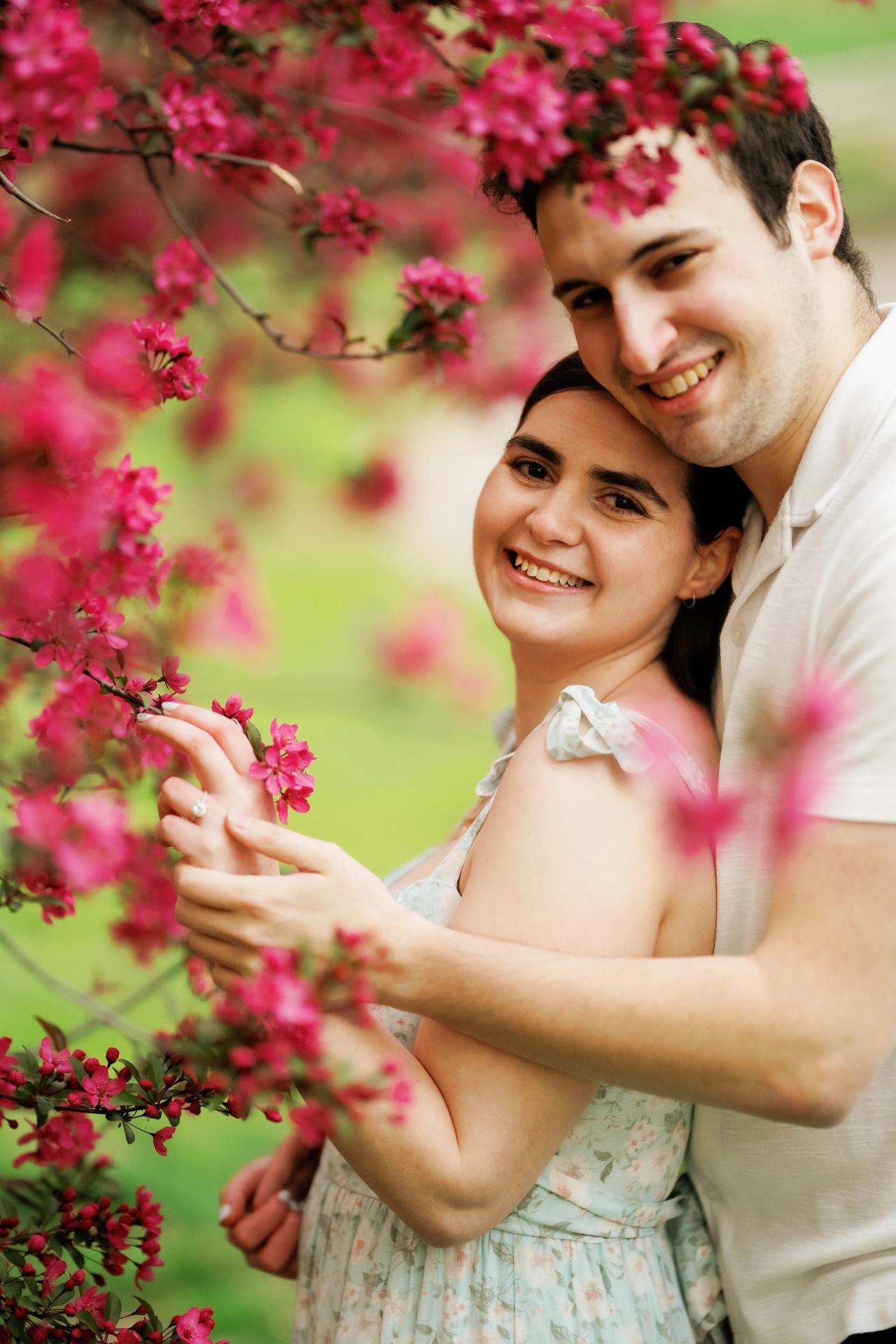 Couple smiling beneath vibrant flowering branches