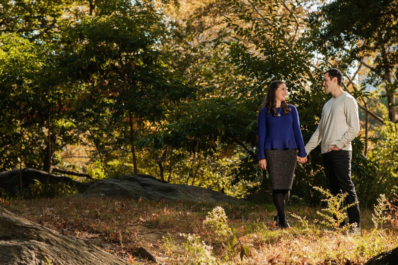 Wide engagement portrait beside rocks beneath autumn trees