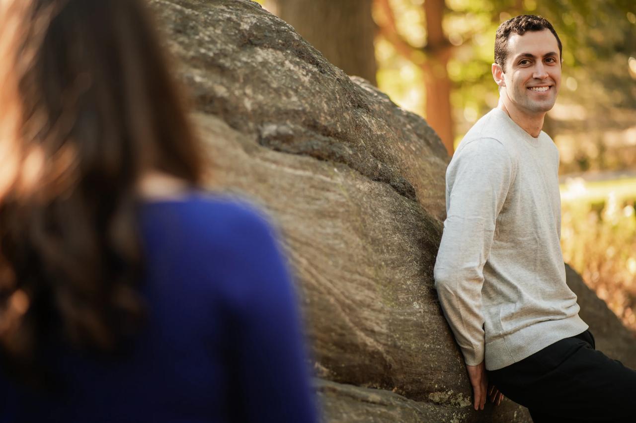 Man smiling toward his partner beside a park boulder