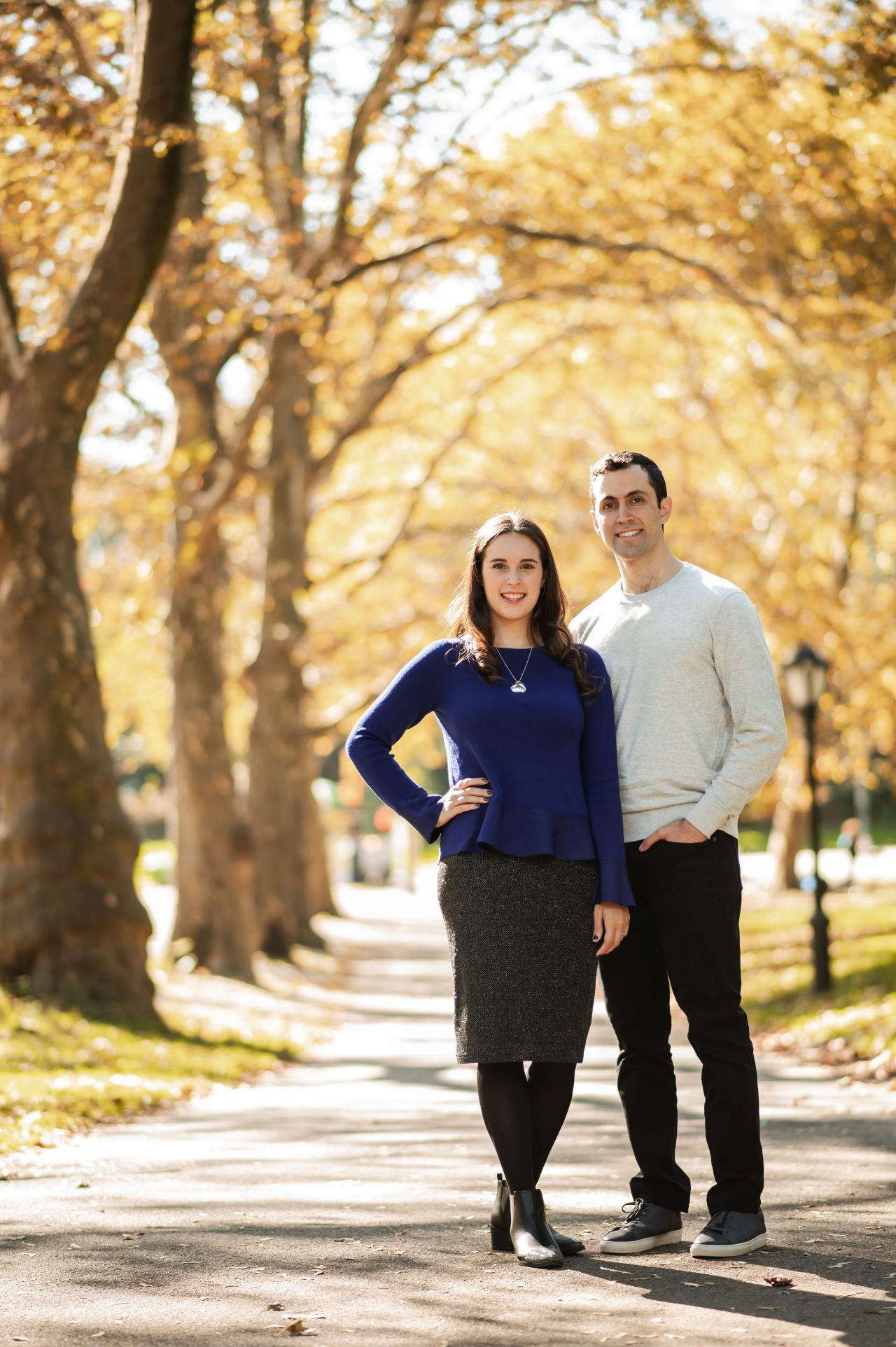 Full-length engagement portrait on a tree-lined park path
