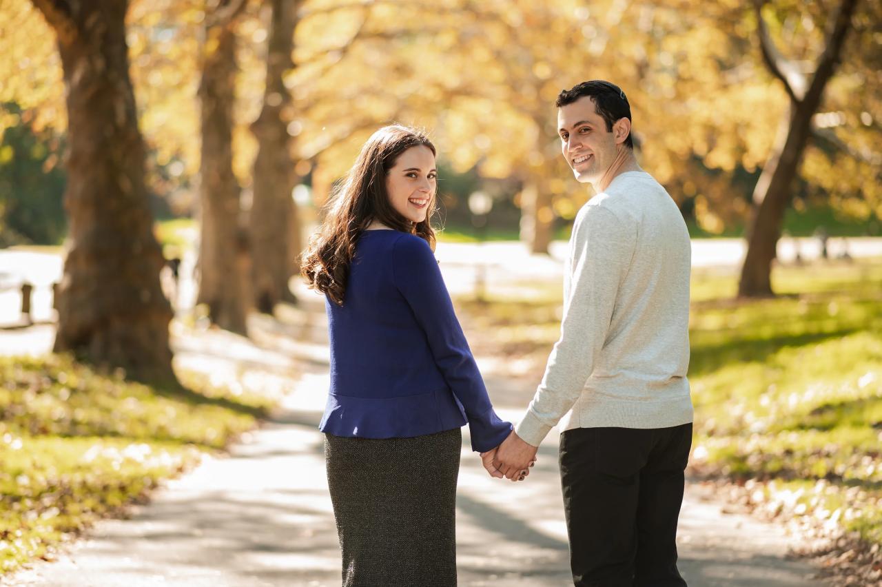 Couple looking back while walking together beneath autumn trees