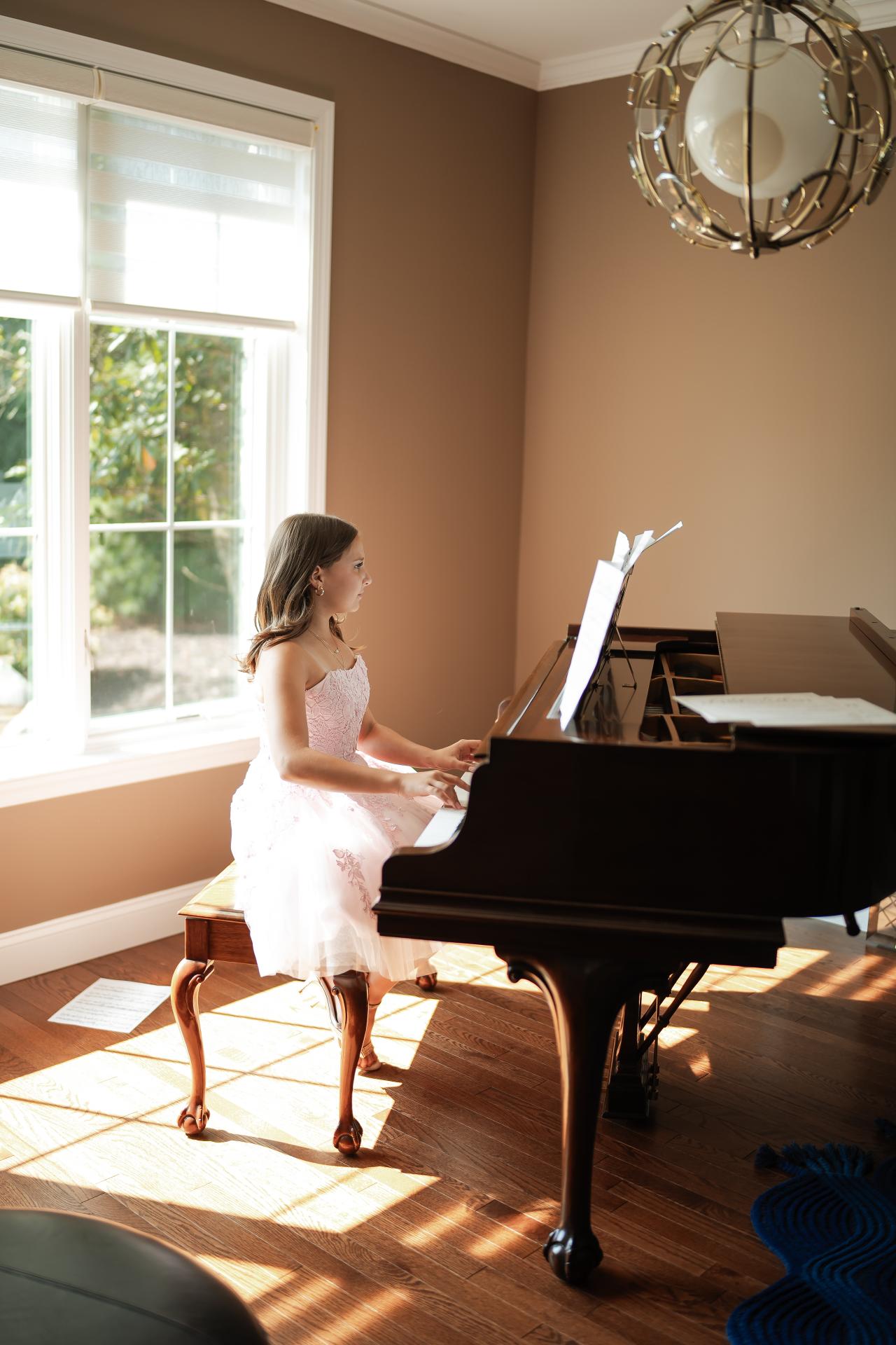 A sister seated at a grand piano in a sunlit room