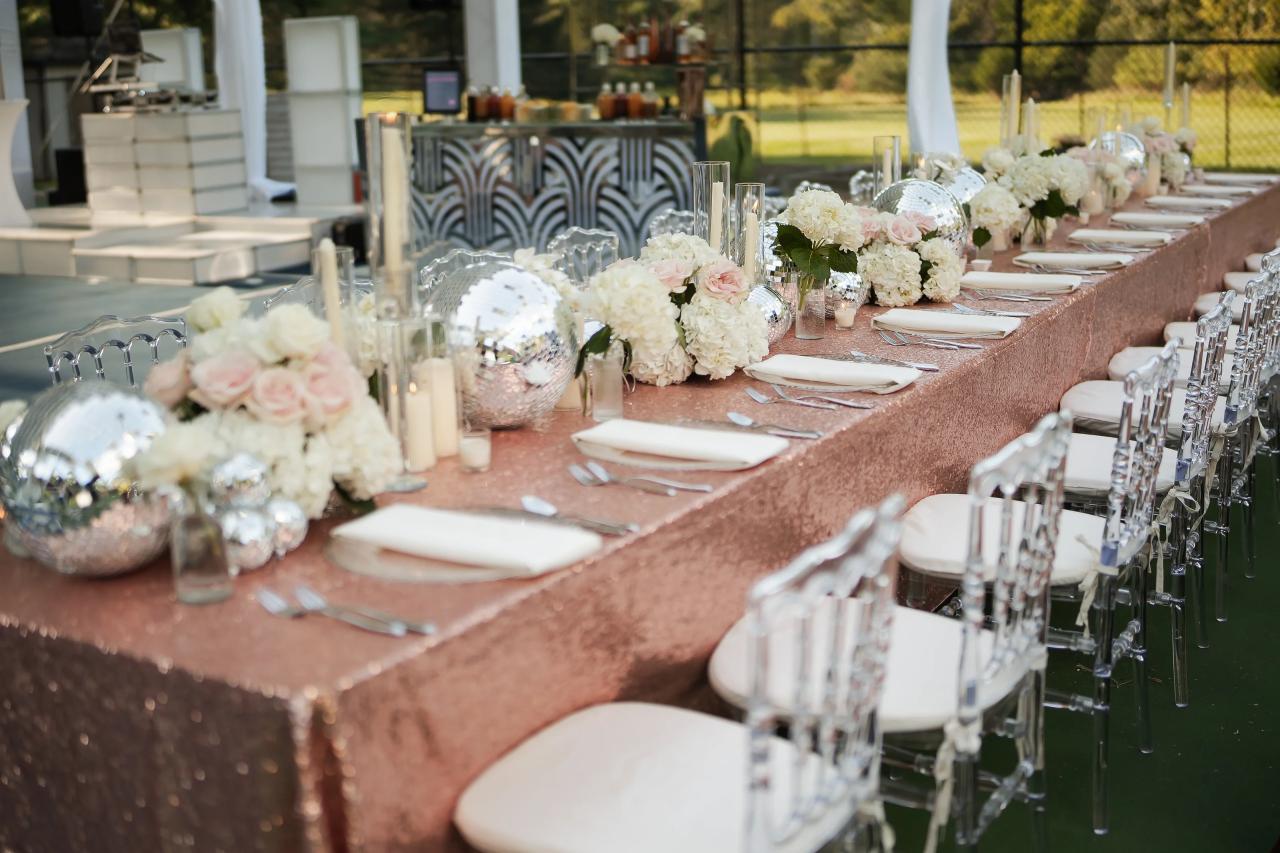 Long reception table with white flowers and pink table linens under a tent