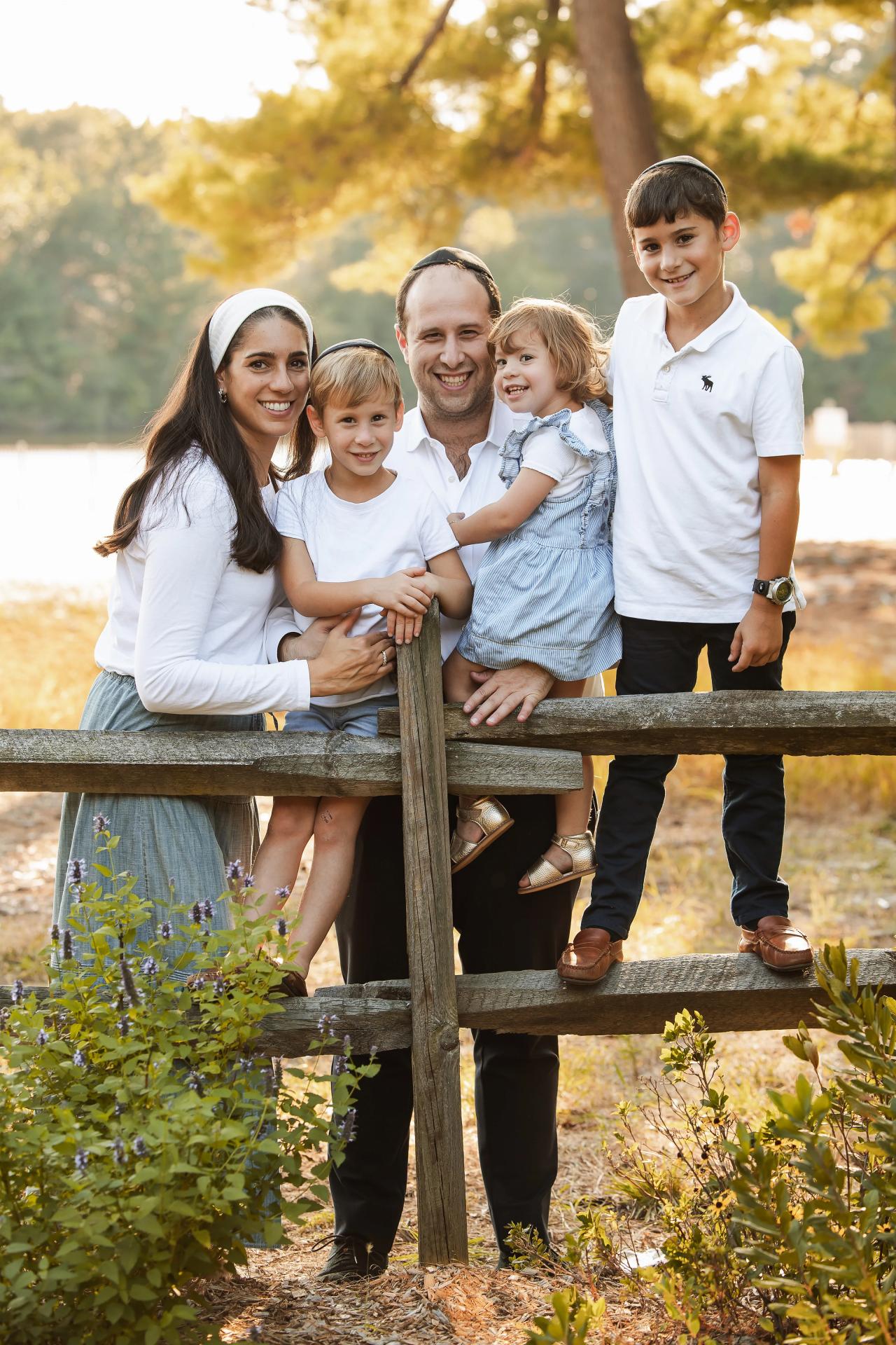Parents and three children gathered at a wooden fence for a fall family portrait