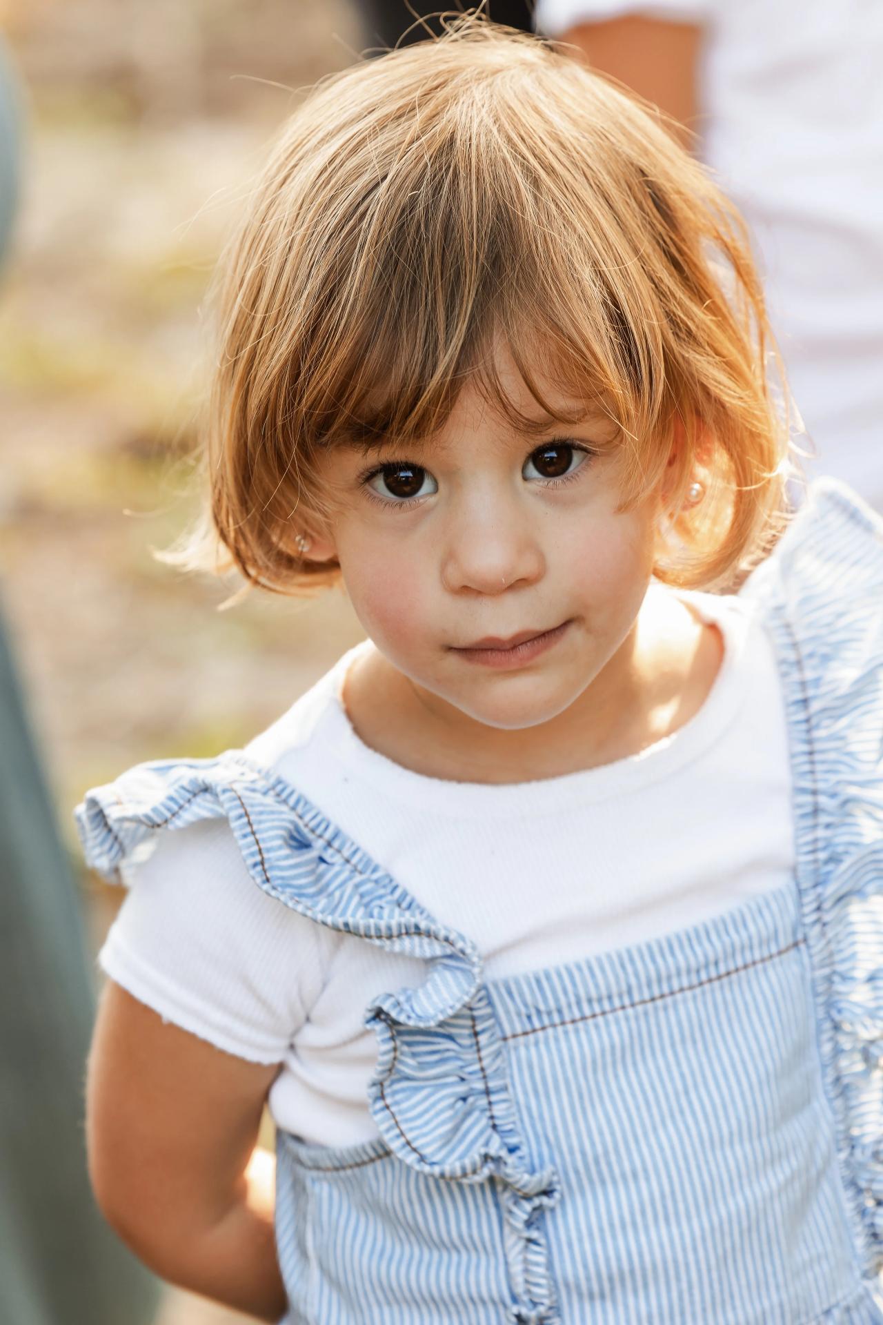 Little girl in a blue dress standing beside a wooden fence