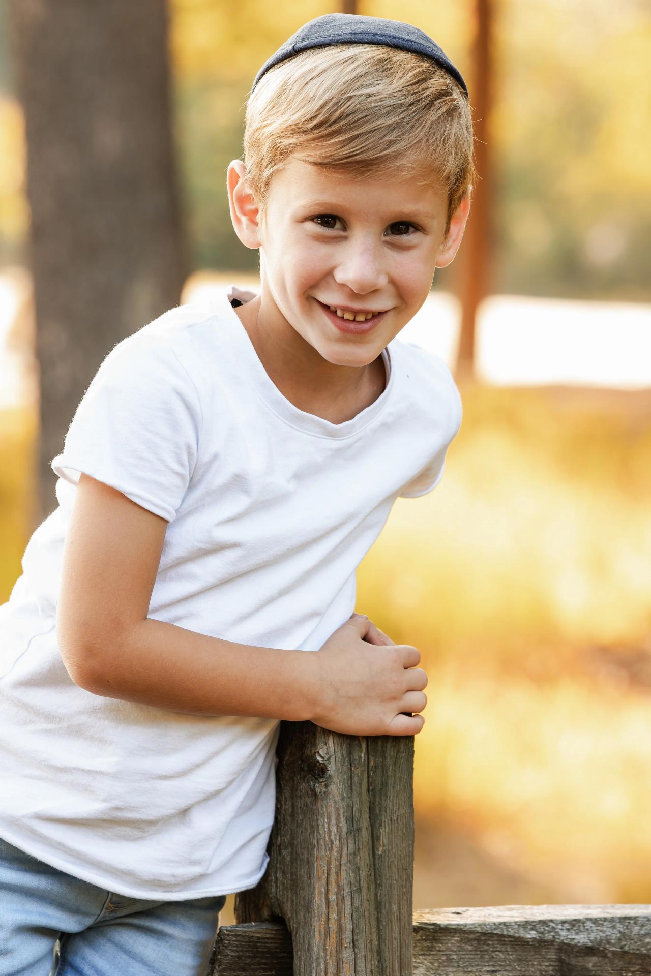 Younger boy in a white polo shirt smiling beside the lakeside fence