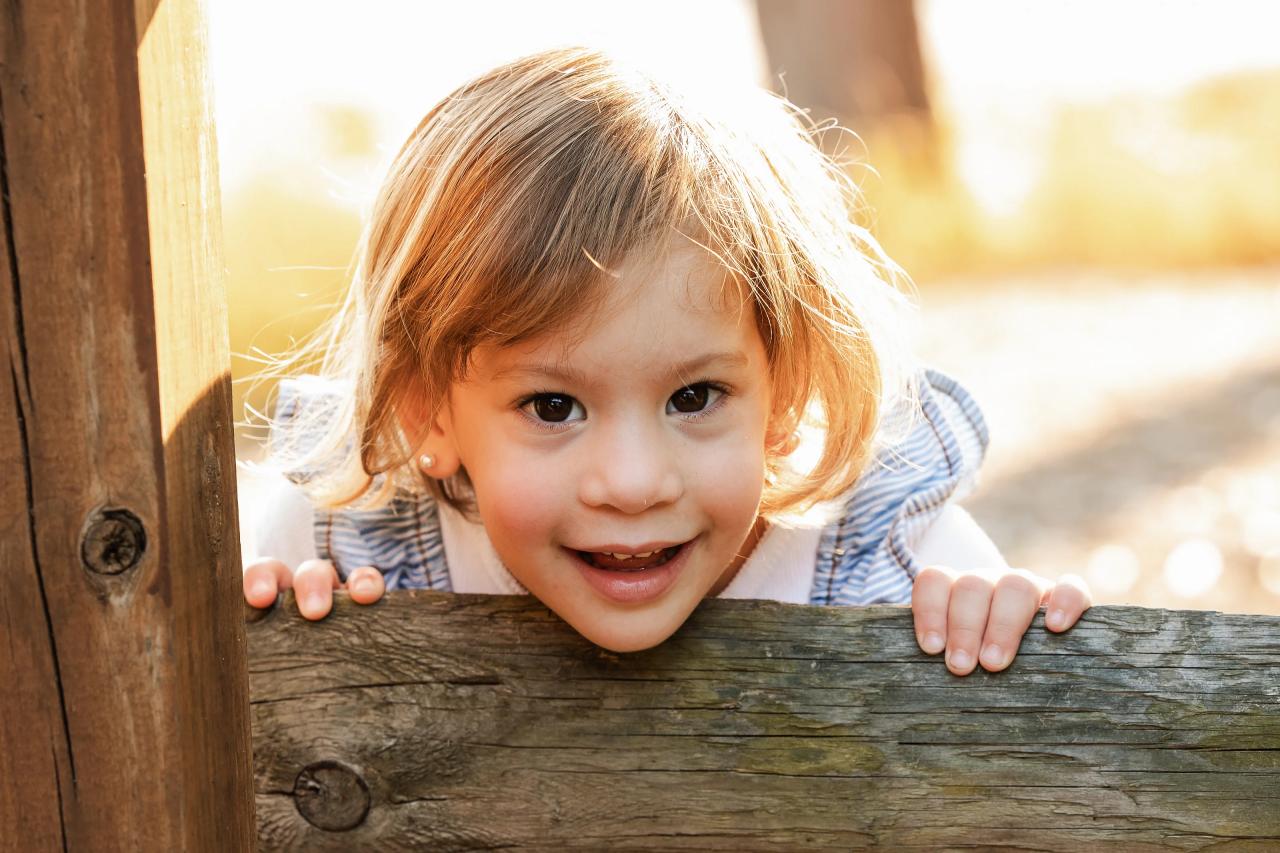 Little girl laughing beside a wooden fence post in the autumn setting