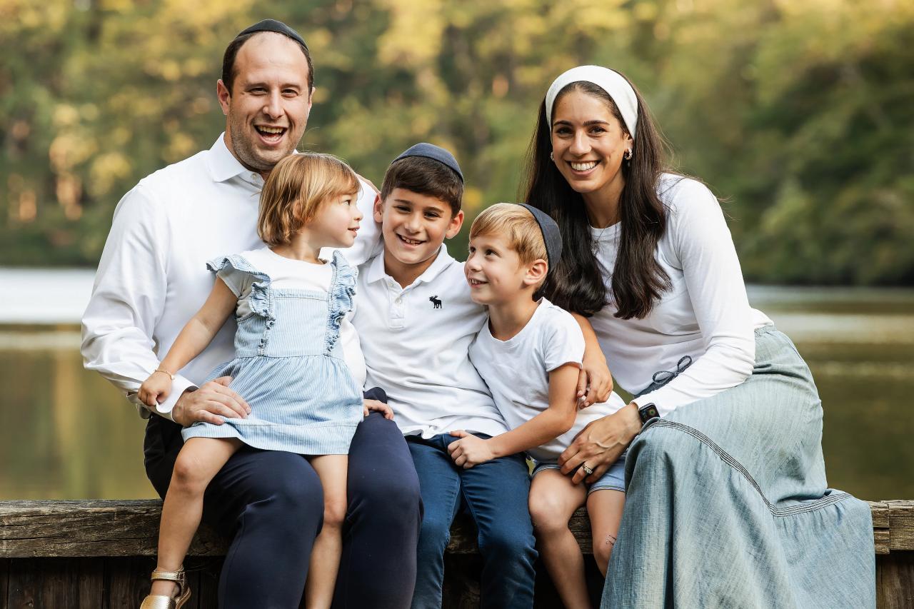 Parents and three children smiling together on a low wall beside the water