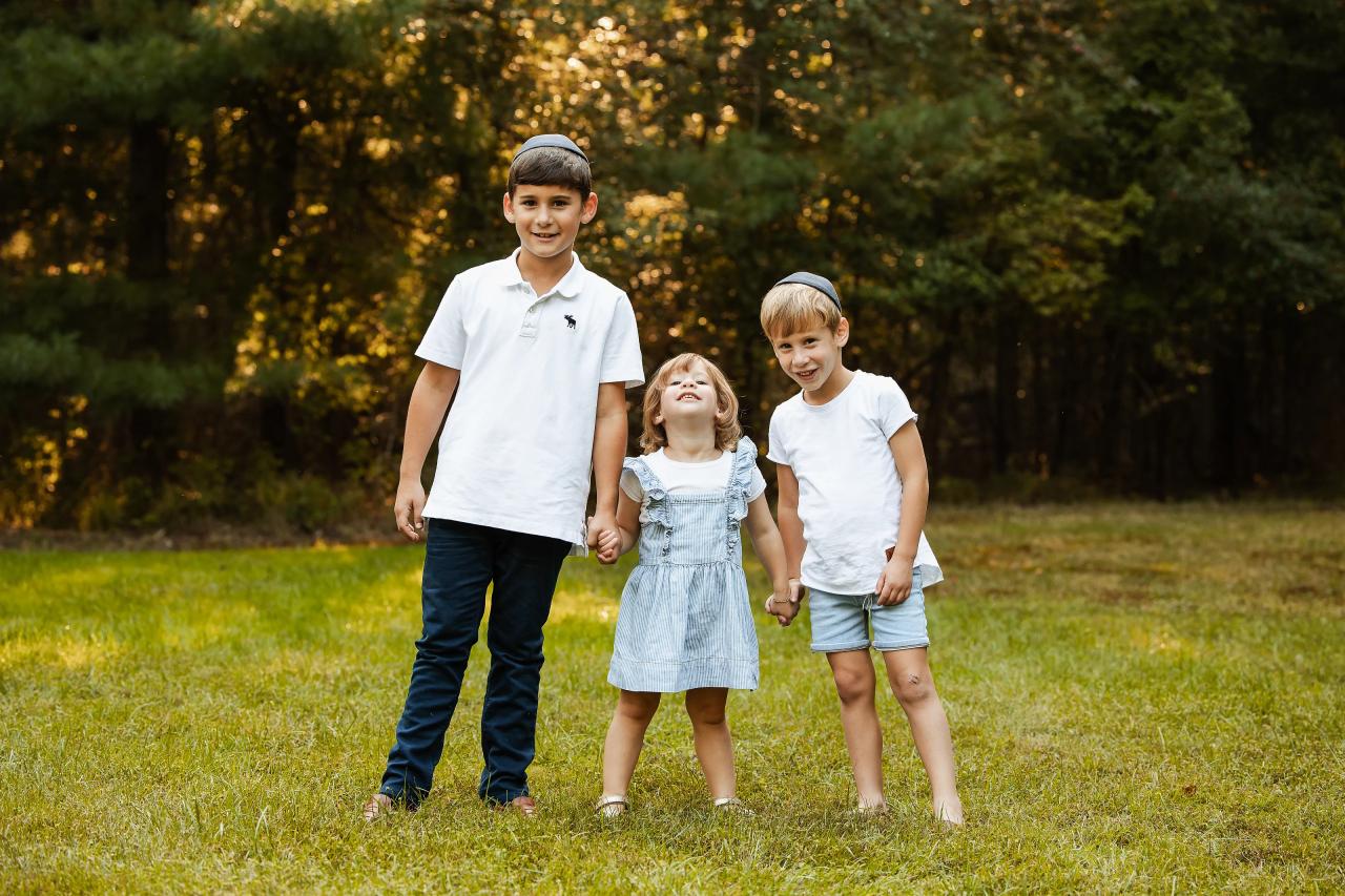 Three siblings smiling together in their outdoor family portrait