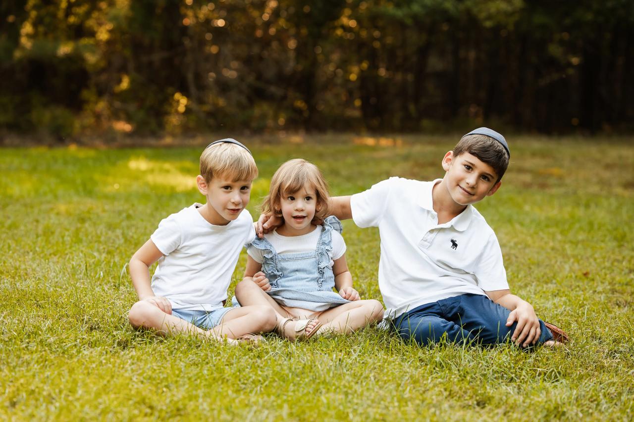 Two boys and their sister seated together and smiling on the grass