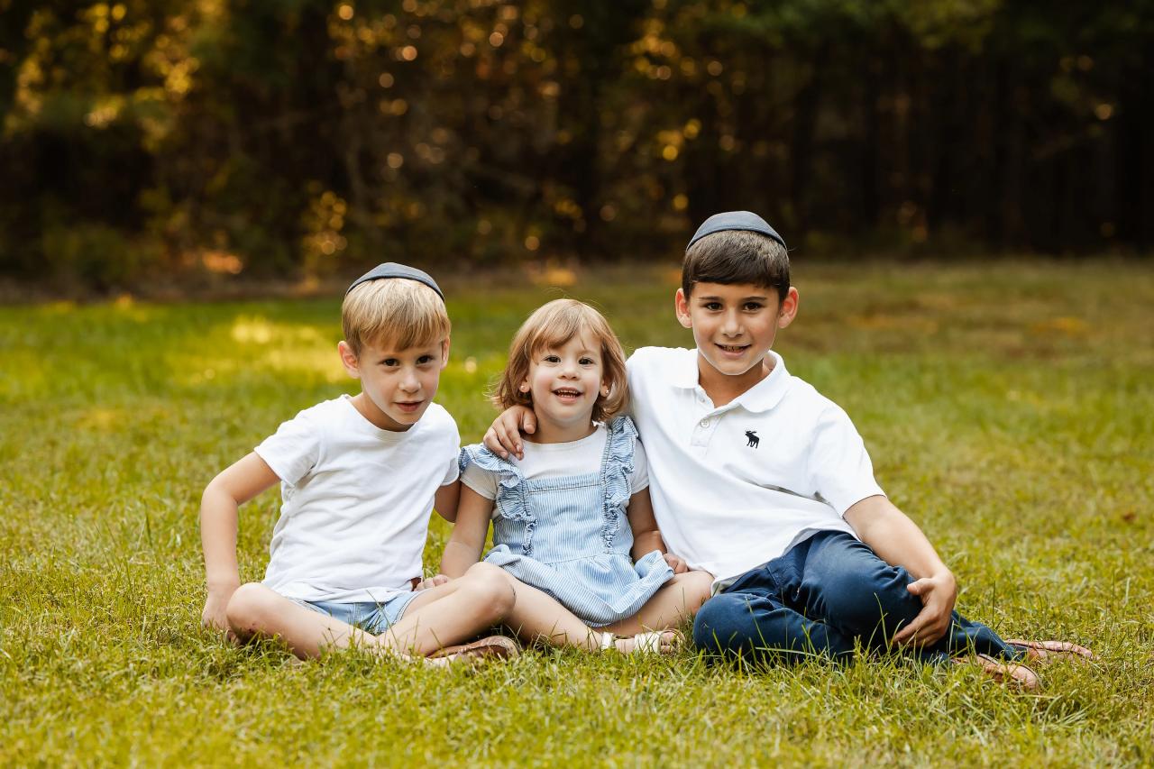 Three siblings gathered closely for a seated portrait on the lawn