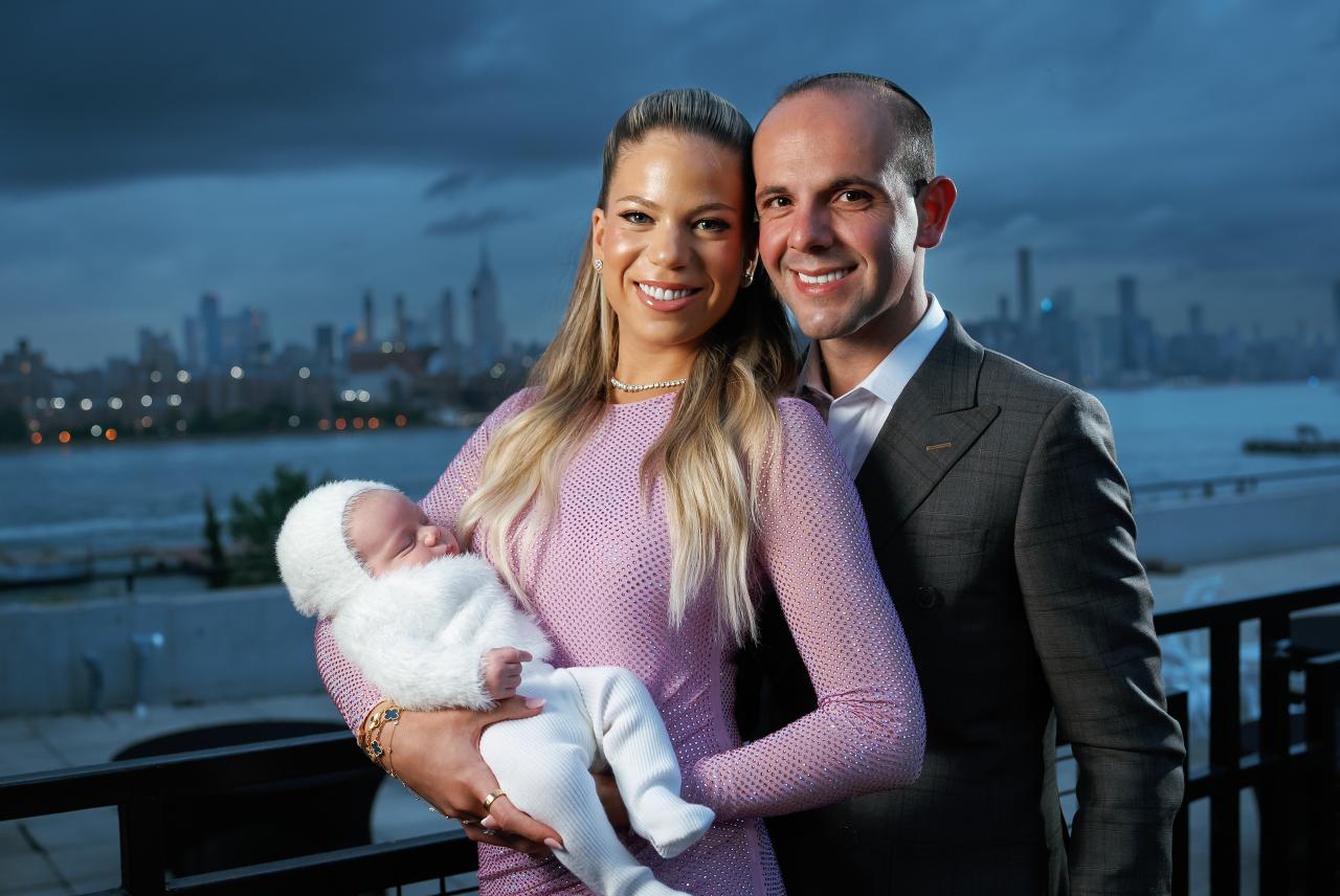 Parents holding their baby beside the river with the city skyline behind them