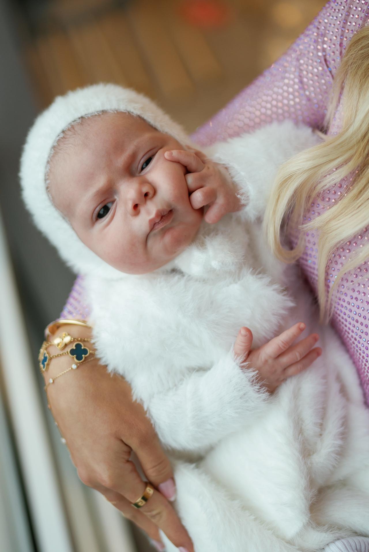 Close portrait of a baby in a white outfit resting in a parent’s arms