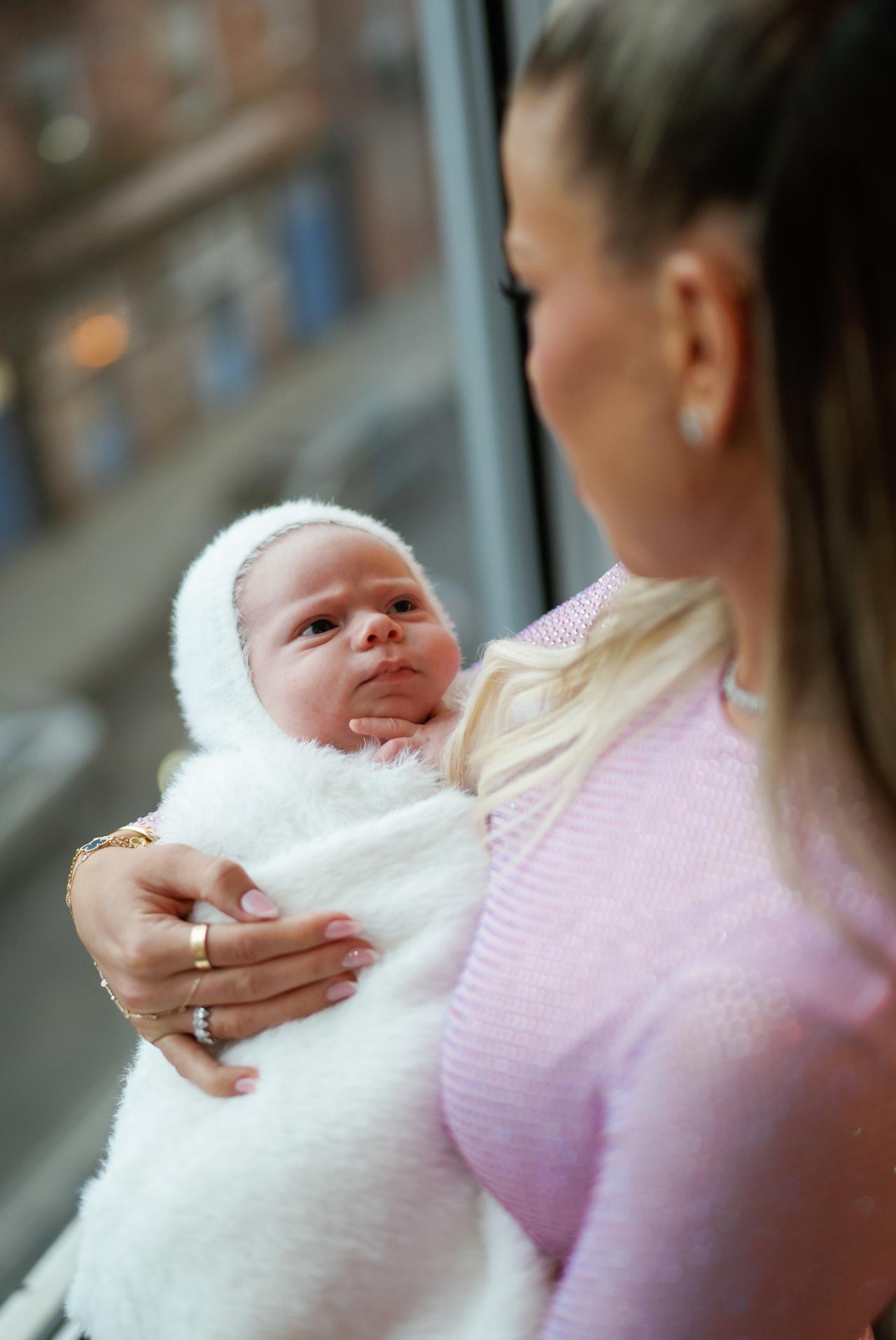 Baby looking up at mother beside a window