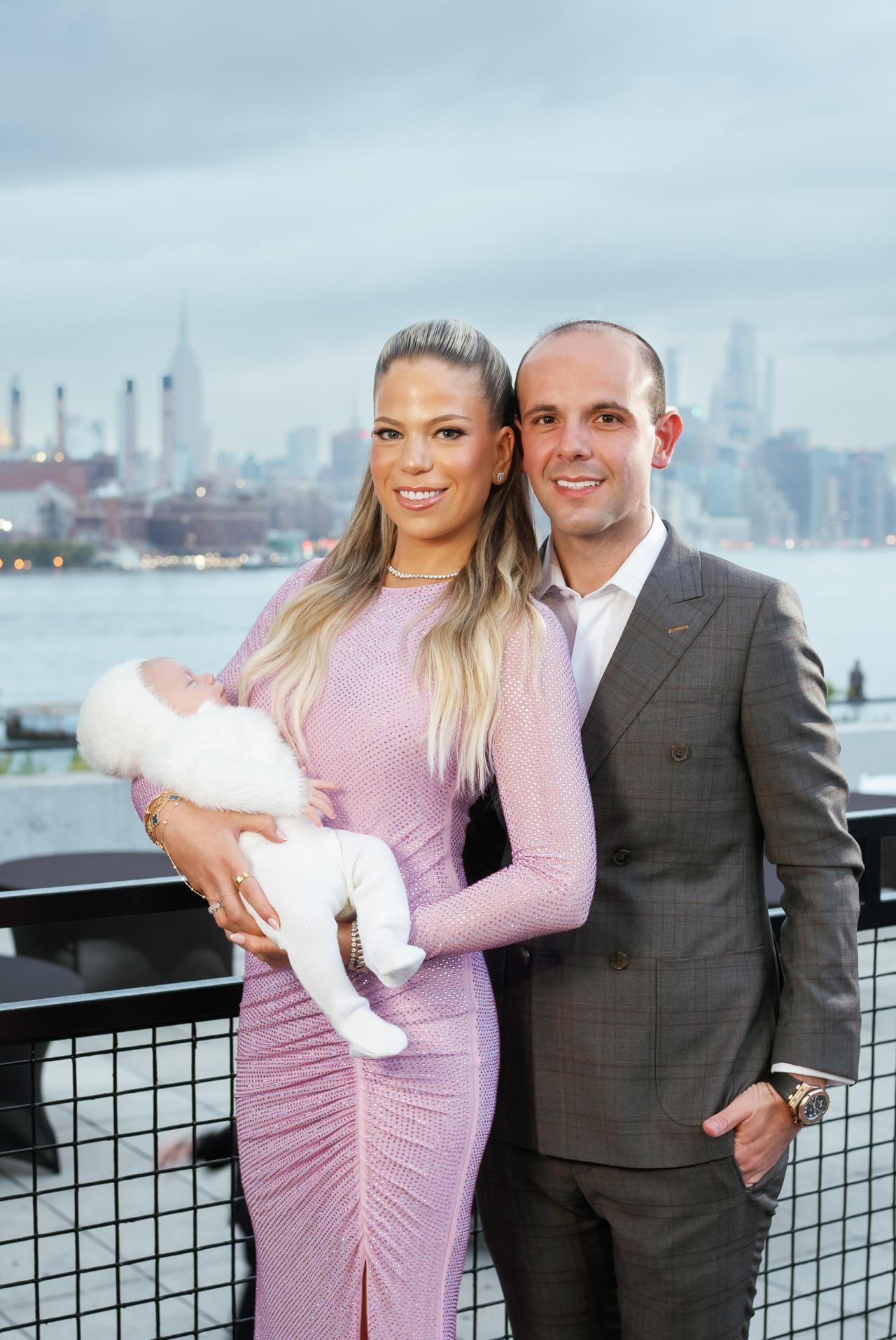 Parents smiling together while holding their baby on the riverside terrace