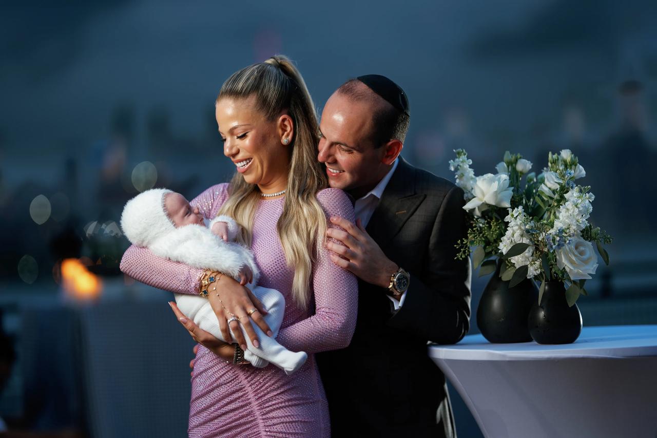 Parents looking down at their baby with evening city lights behind them
