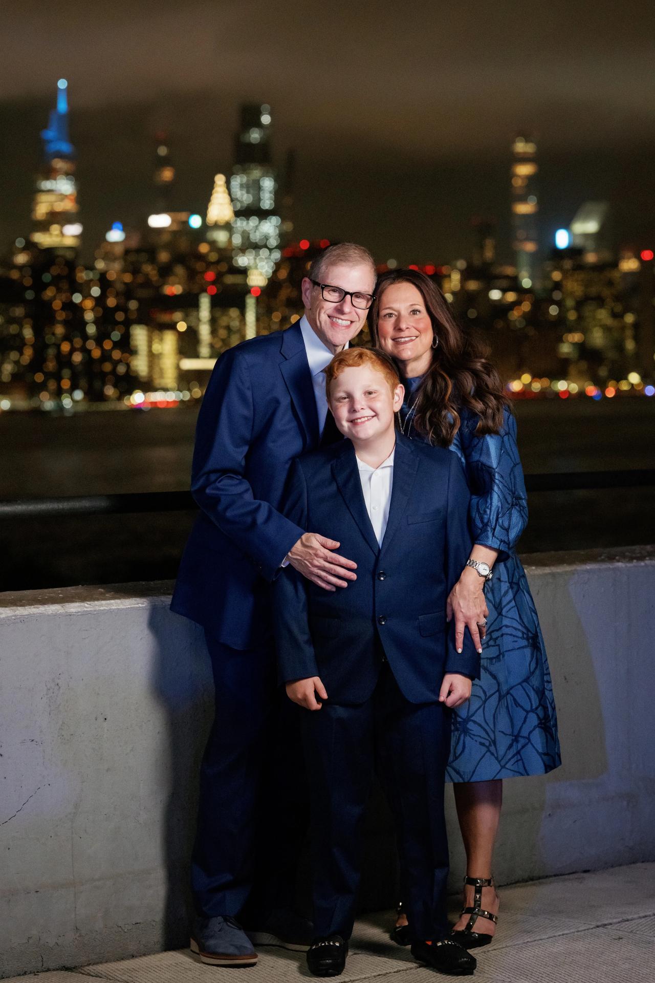 Three family members smiling together against the evening skyline