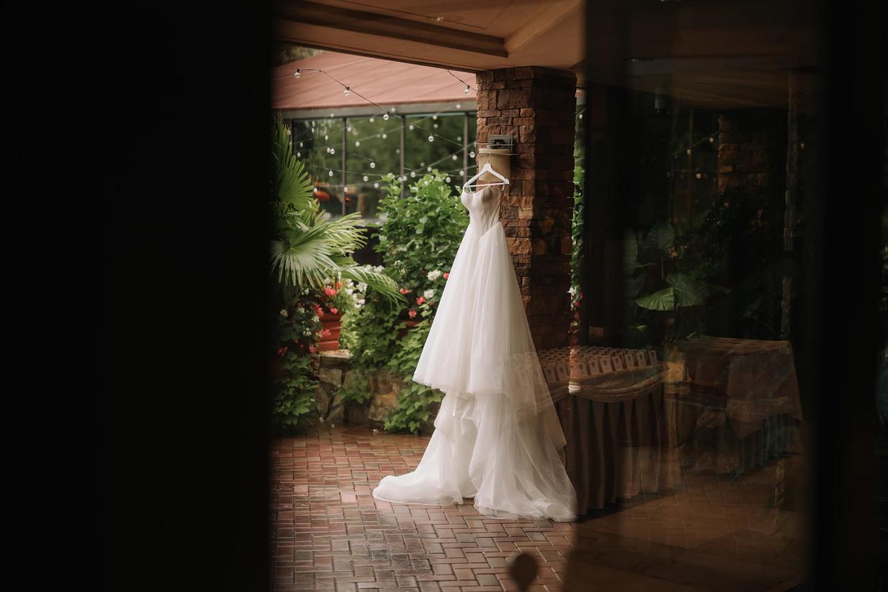 Wedding dress hanging beside a sunlit garden window. Crest Hollow wedding in Woodbury, Long Island.