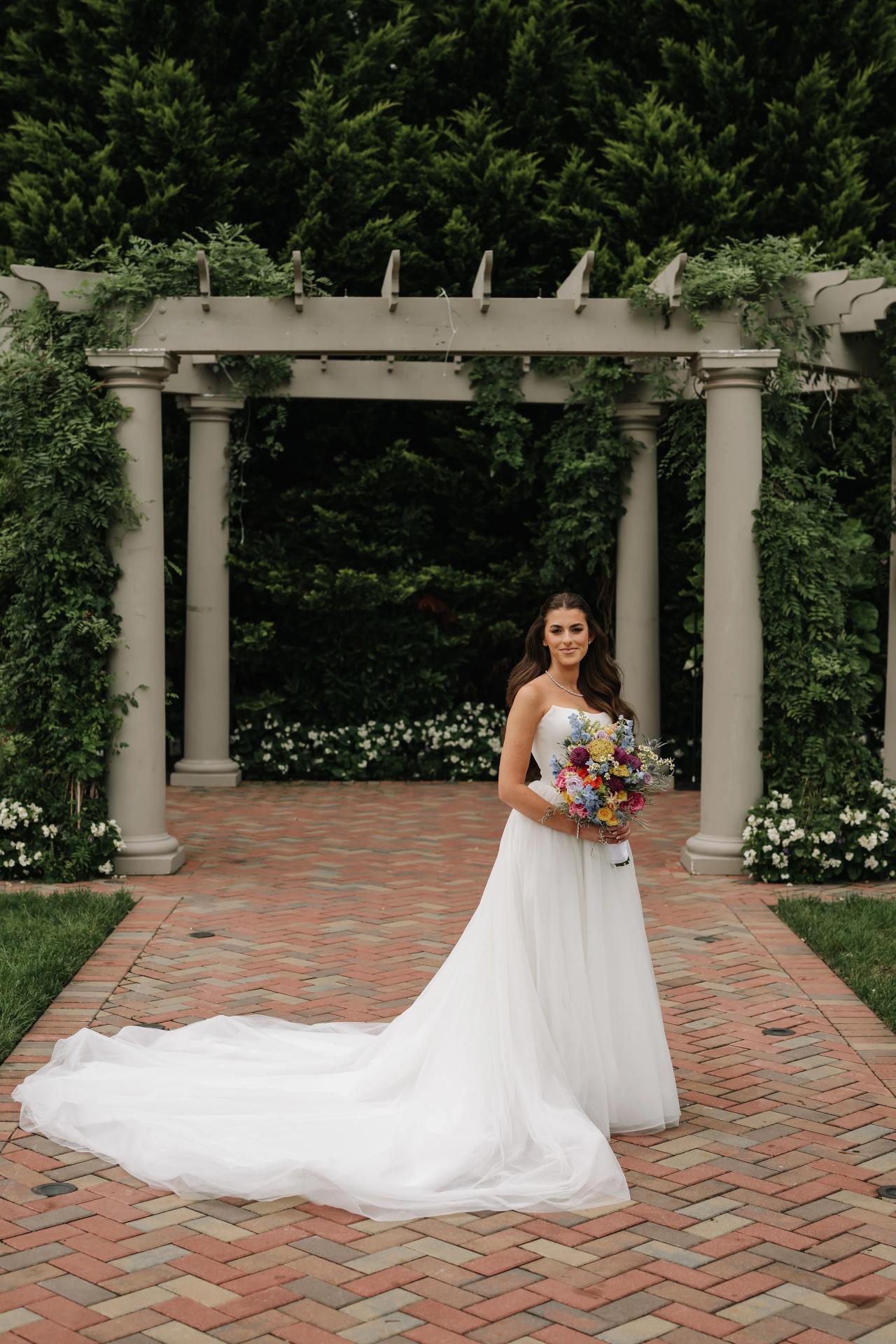 Full-length bridal portrait beneath a garden pergola. Crest Hollow wedding in Woodbury, Long Island.