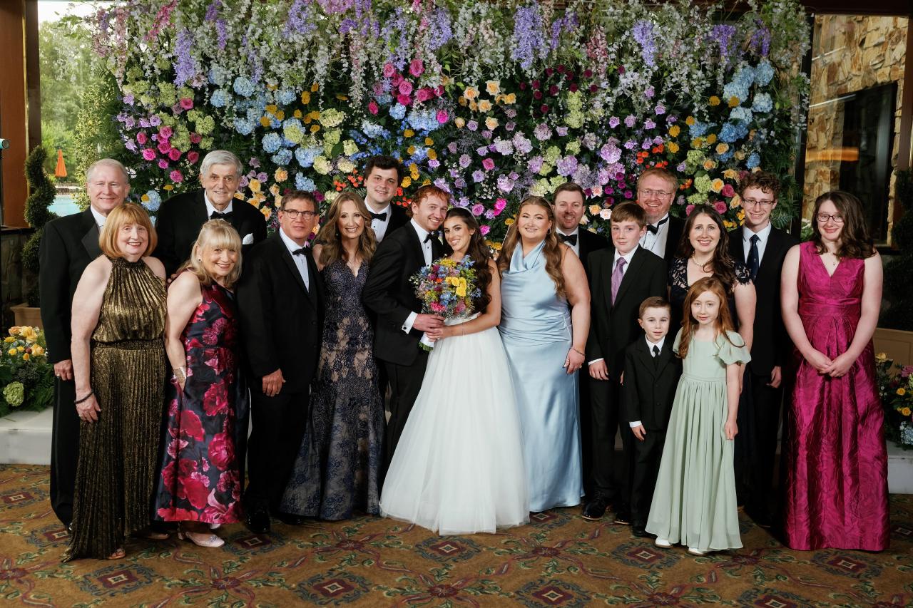 Wedding couple with their extended family beneath a floral wall. Crest Hollow wedding in Woodbury, Long Island.
