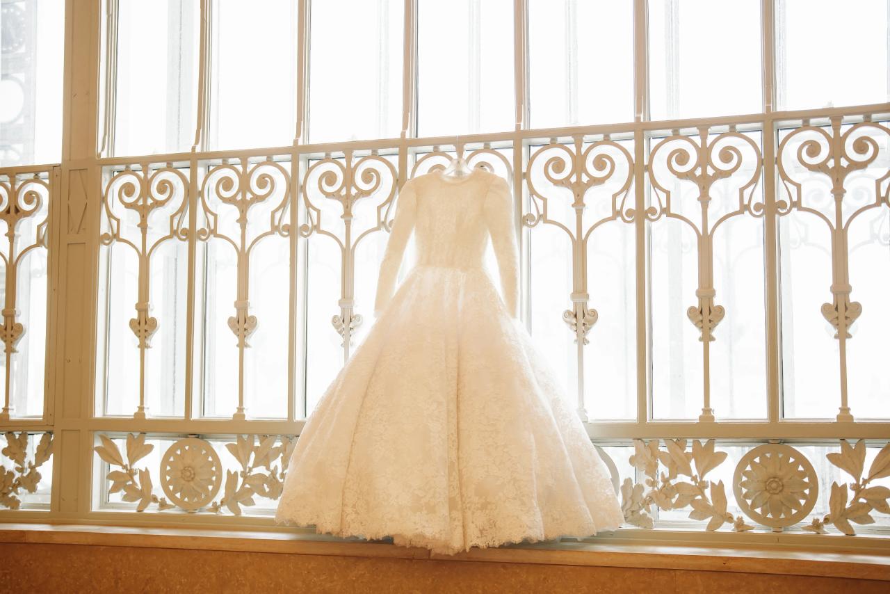 Wedding dress hanging before a tall ornate window. Jewish wedding in Detroit.