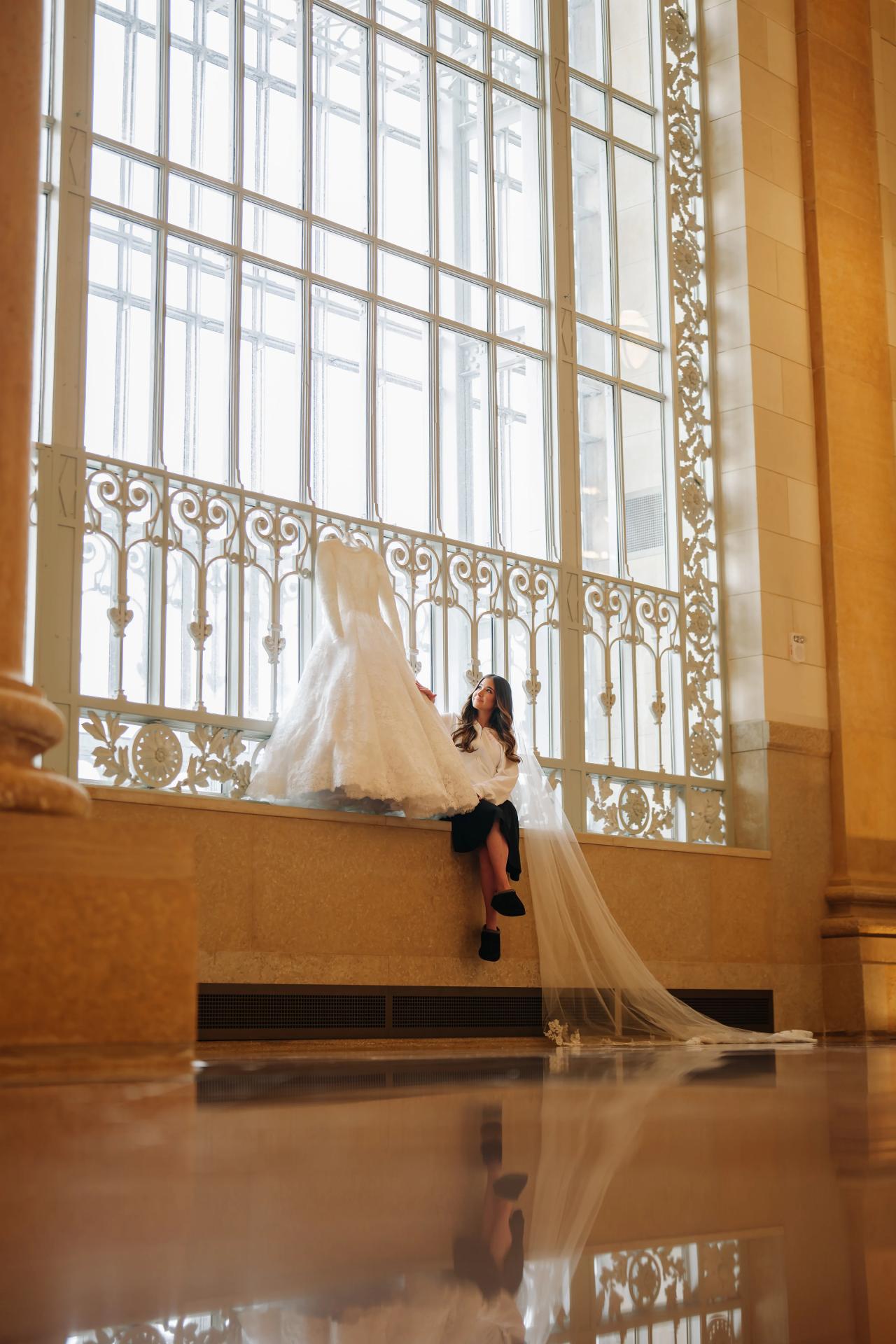 Bride reflected in the floor beside her hanging wedding dress. Jewish wedding in Detroit.