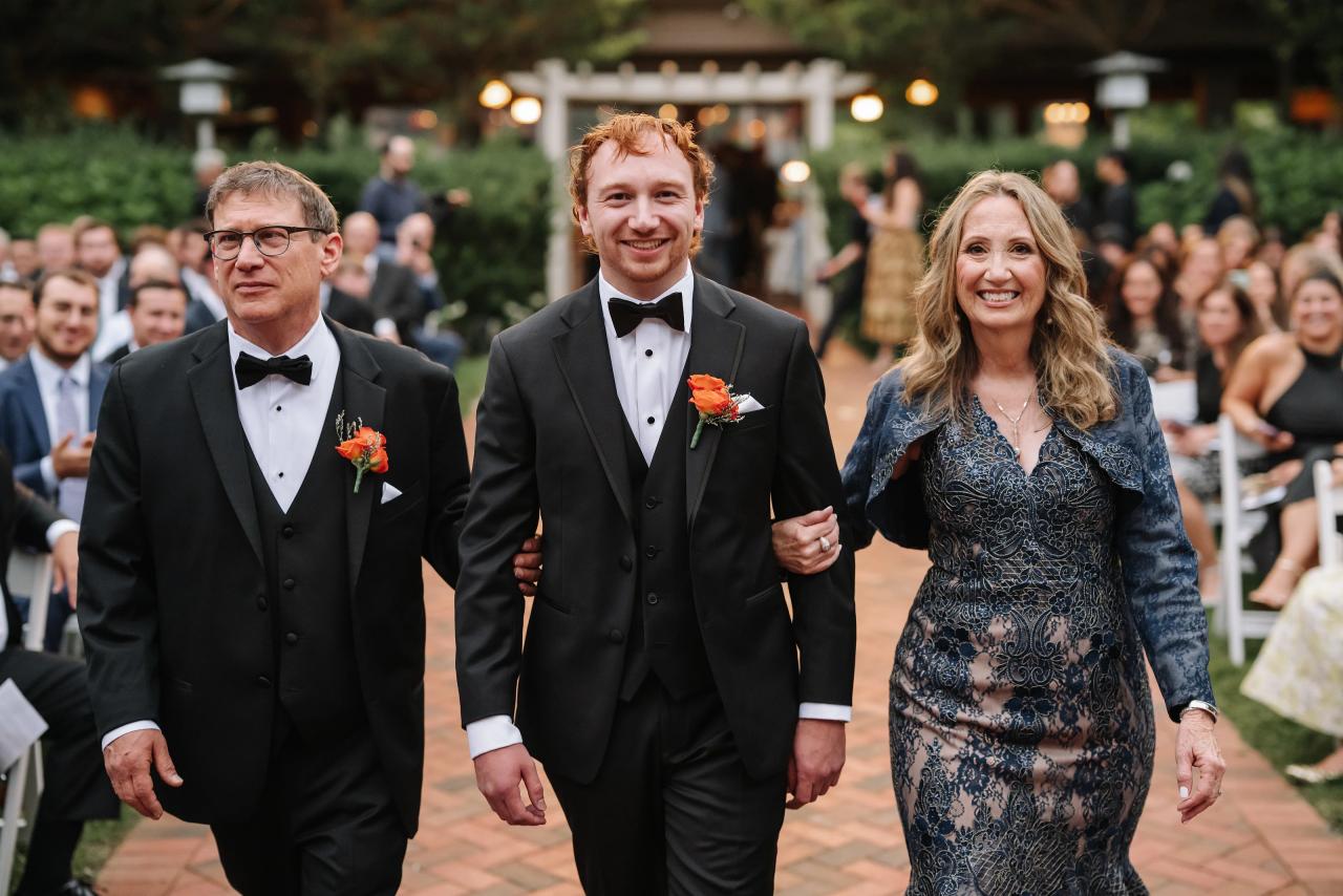 Groom walking down the outdoor wedding aisle with family. Crest Hollow wedding in Woodbury, Long Island.