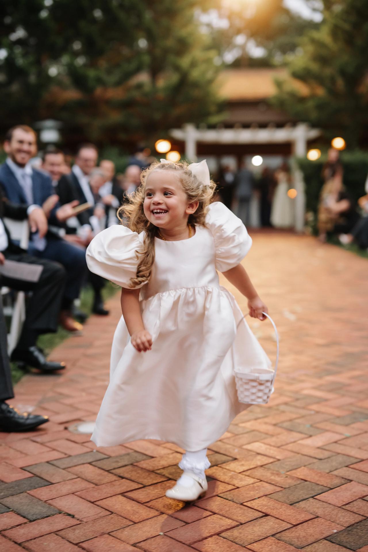 Young flower girl running down the garden aisle. Crest Hollow wedding in Woodbury, Long Island.