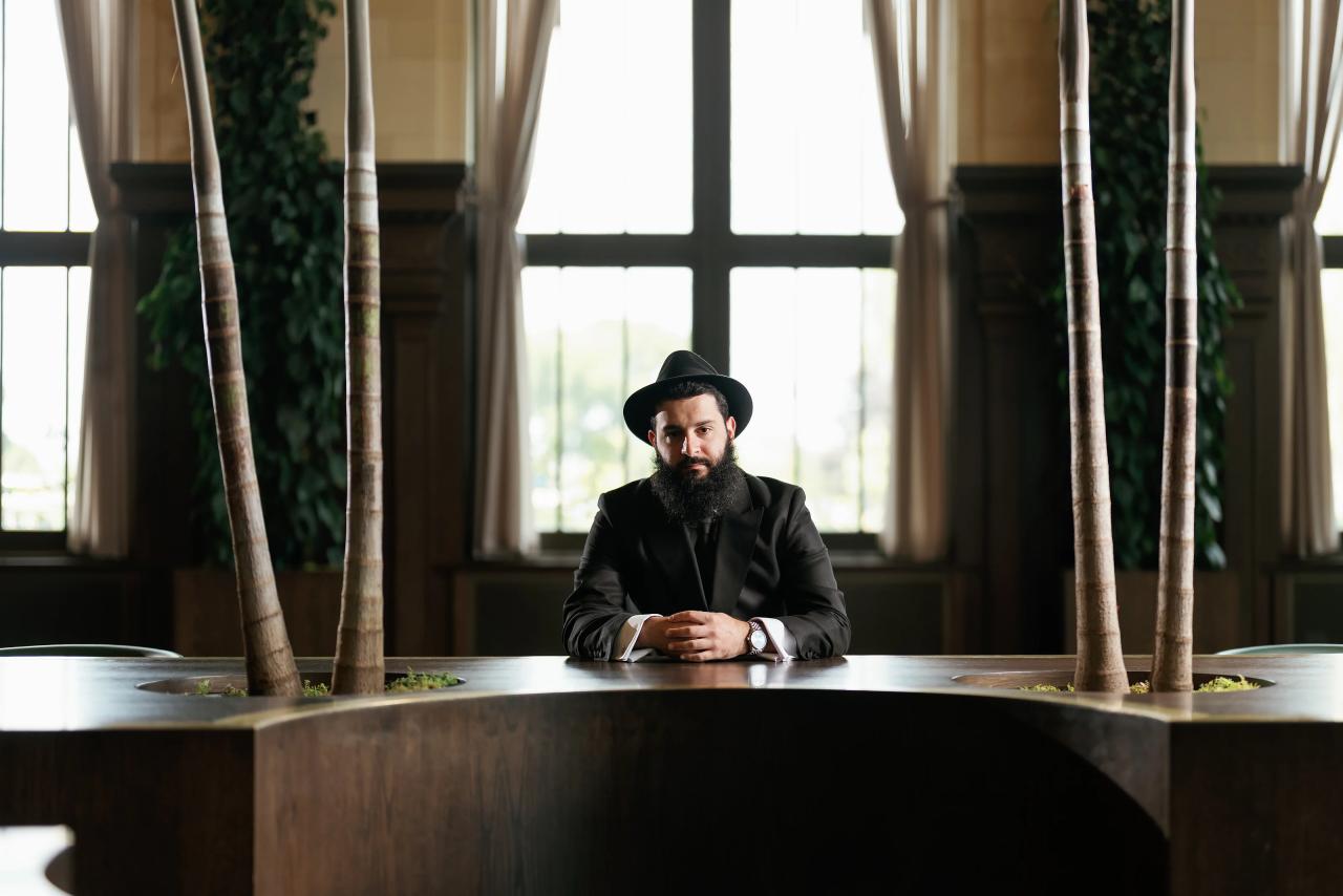 Groom seated at a table beneath a large window. Jewish wedding in Detroit.