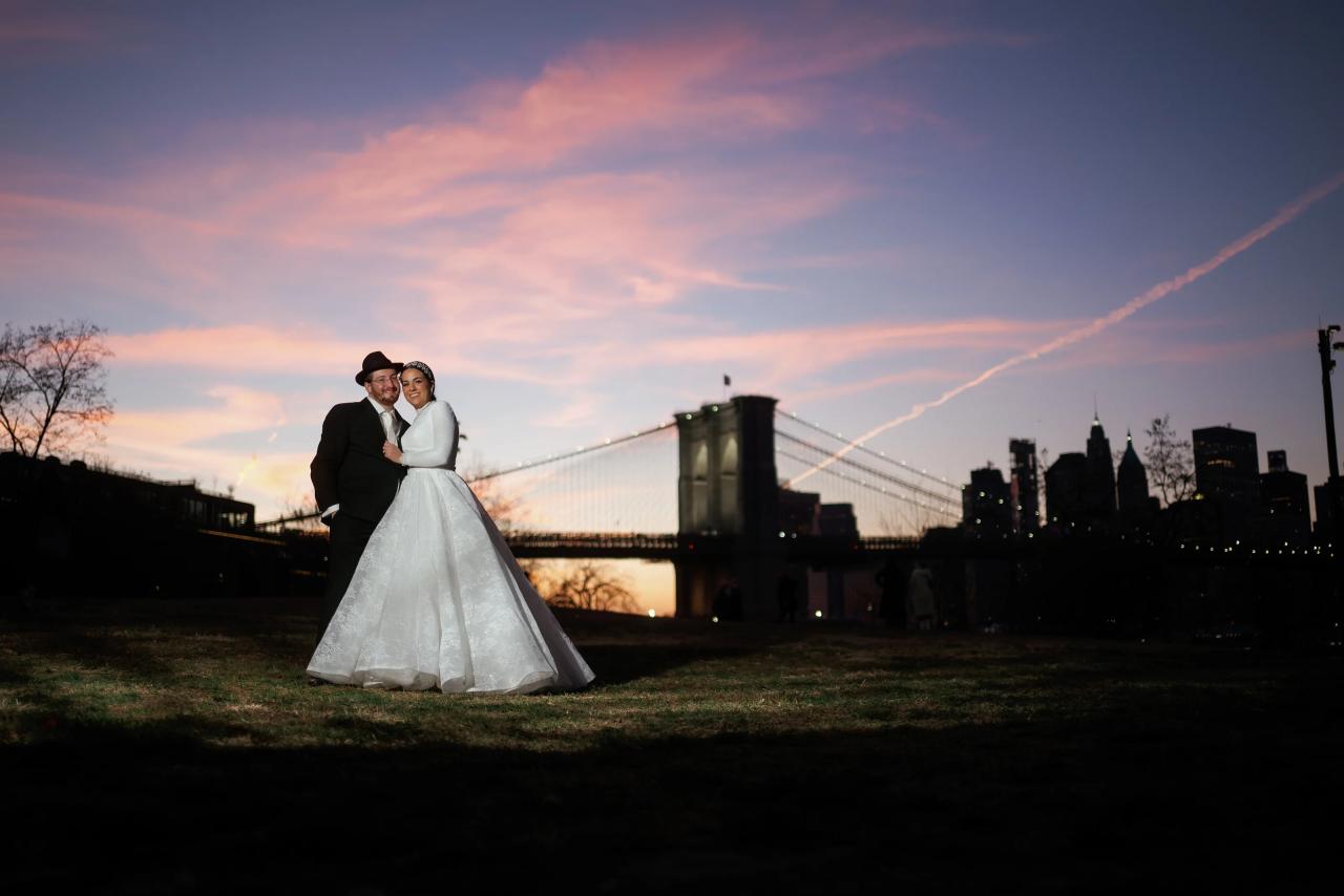 Bride and groom beneath a pink sunset beside the Brooklyn Bridge