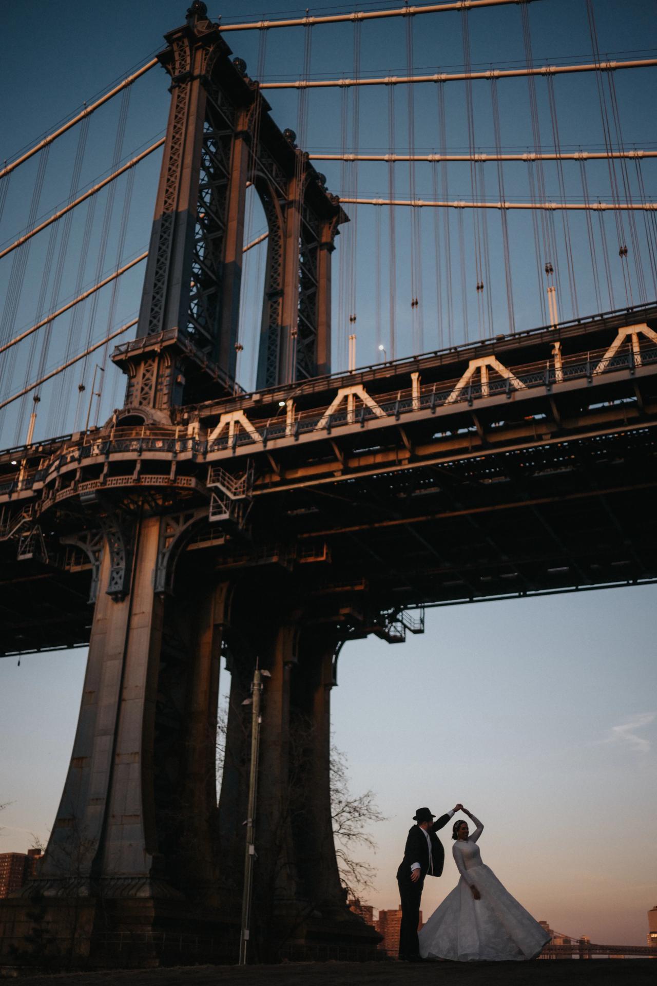 Wedding couple beneath the tower and cables of the Manhattan Bridge. Wedding portraits in Brooklyn, NYC.