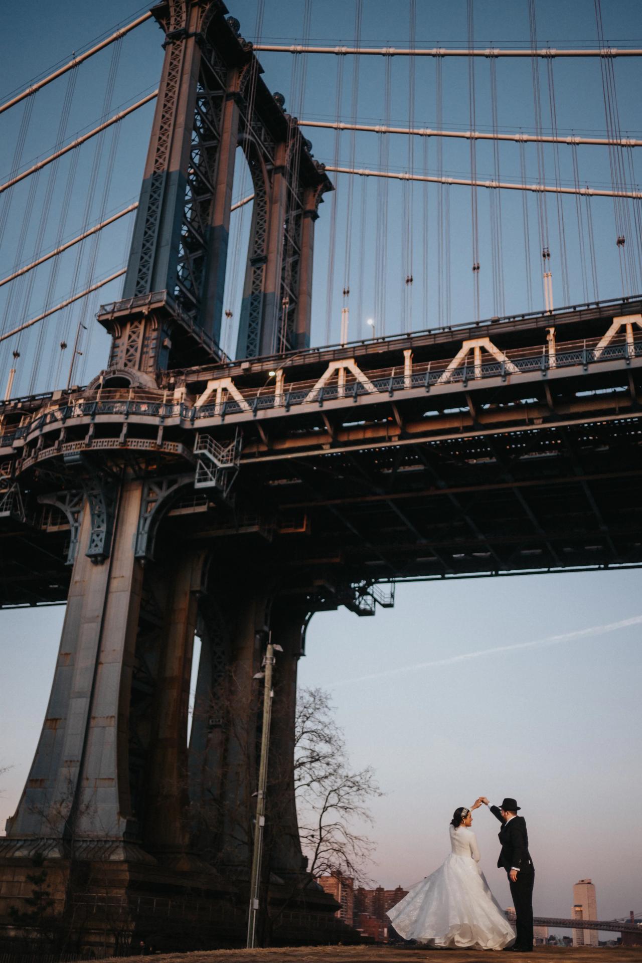 Wedding couple kissing beneath a towering suspension bridge. Wedding portraits in Brooklyn, NYC.