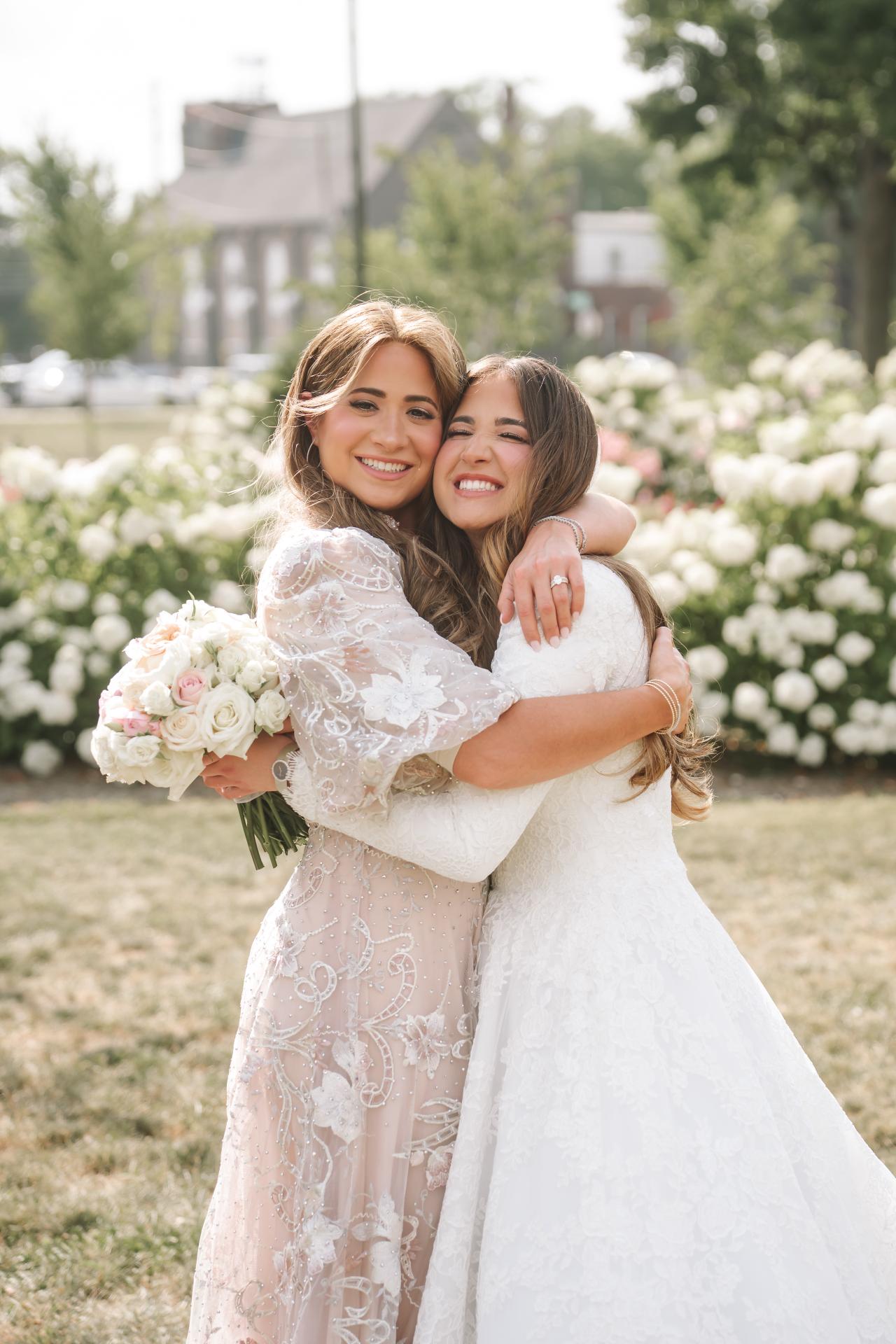 Bride hugging a close family member beside white flowers. Jewish wedding in Detroit.