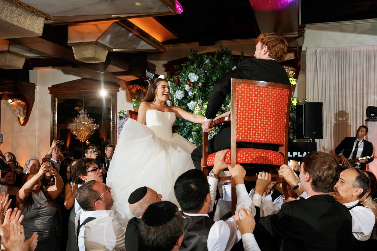 Bride lifted on a chair amid cheering wedding guests. Crest Hollow wedding in Woodbury, Long Island.