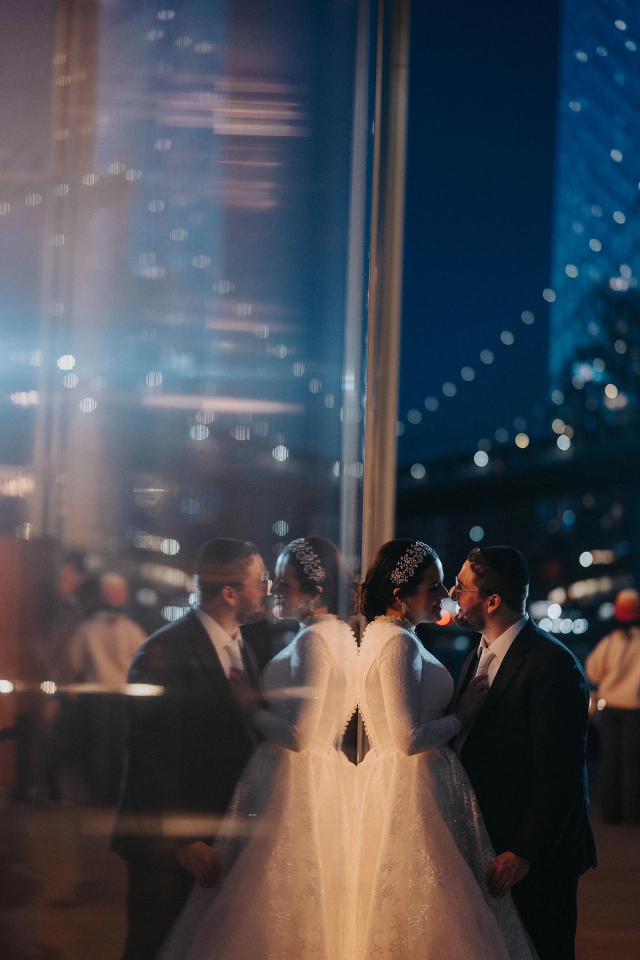 Bride and groom reflected beside the glowing carousel. Wedding portraits in Brooklyn, NYC.