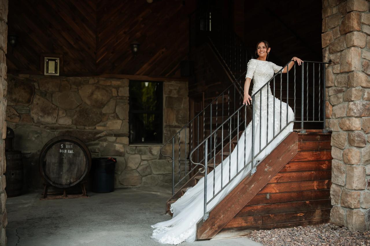 Bride on a rustic staircase beneath the barn’s timber beams. Wedding at Indian Ridge.