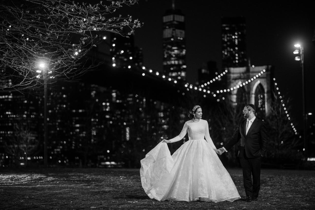Black-and-white wedding portrait with bridge and city lights. Wedding portraits in Brooklyn, NYC.