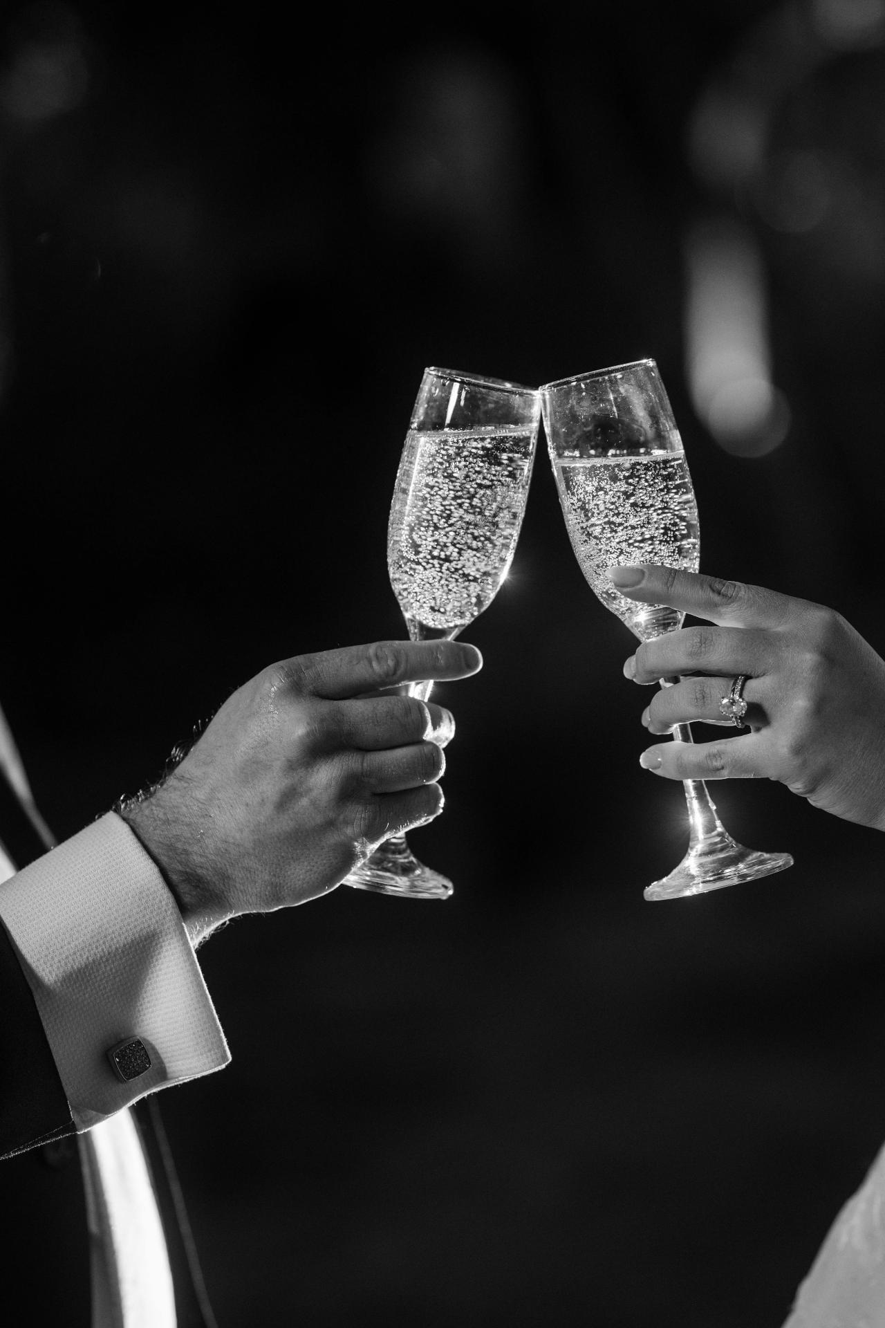 Black-and-white detail of wedding champagne glasses raised together. Wedding portraits in Brooklyn, NYC.