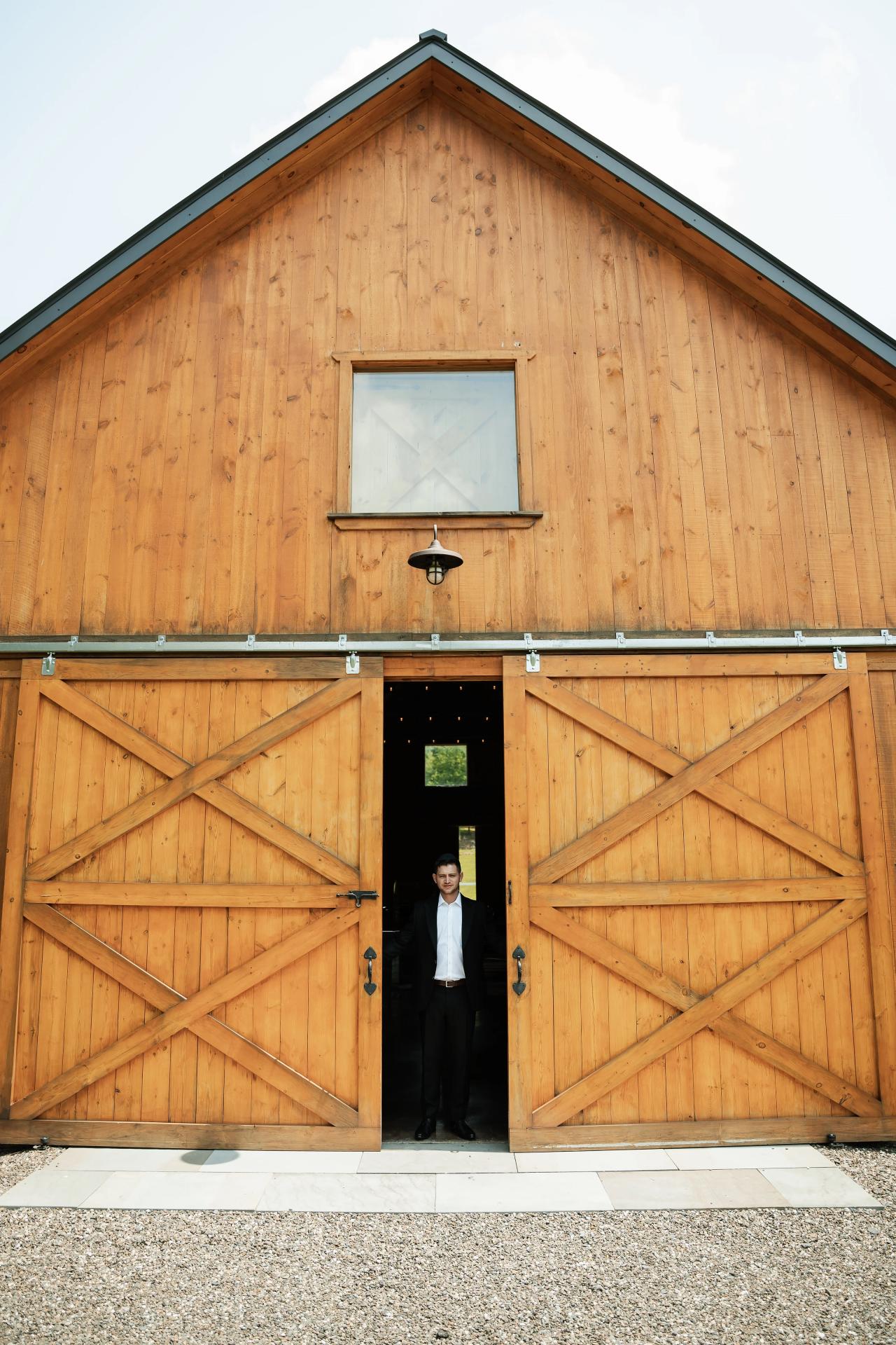 Wide portrait of the groom at the wooden barn doors. Wedding at Indian Ridge.