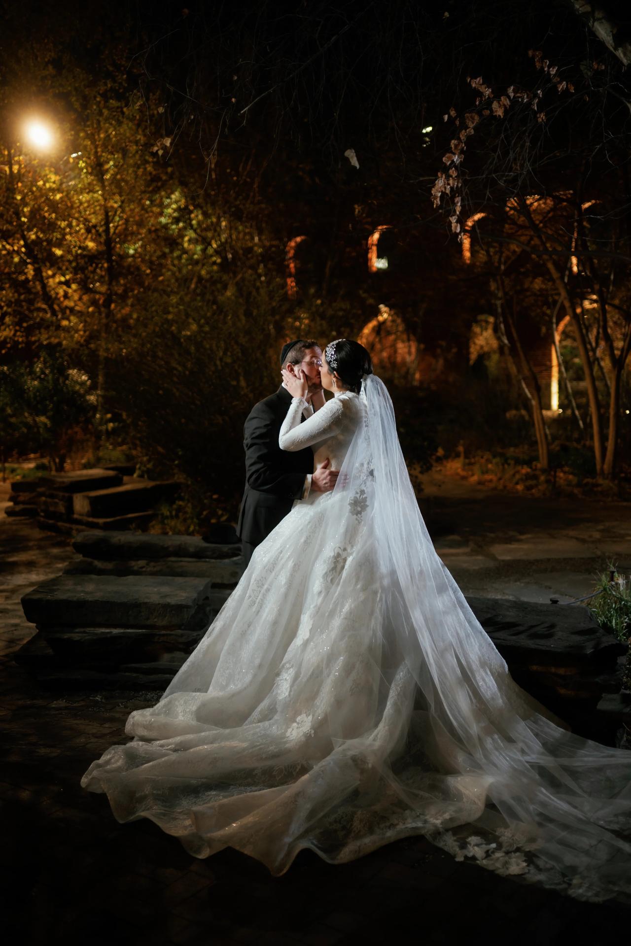 Wedding couple embracing with the bridal train spread across a path. Wedding portraits in Brooklyn, NYC.