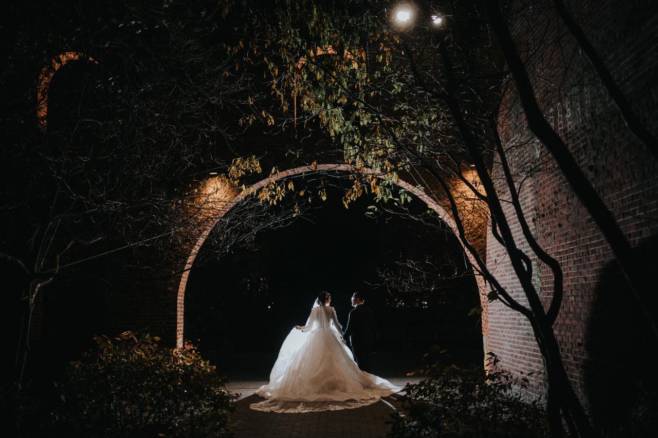 Bride and groom framed by a brick garden arch at night. Wedding portraits in Brooklyn, NYC.