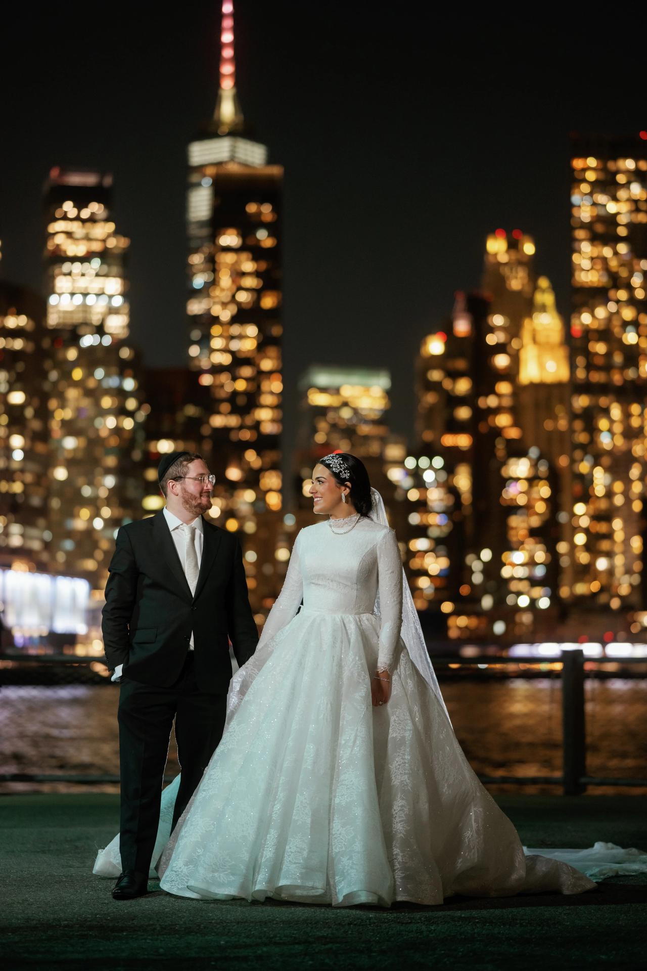 Bride and groom standing together against Manhattan city lights. Wedding portraits in Brooklyn, NYC.